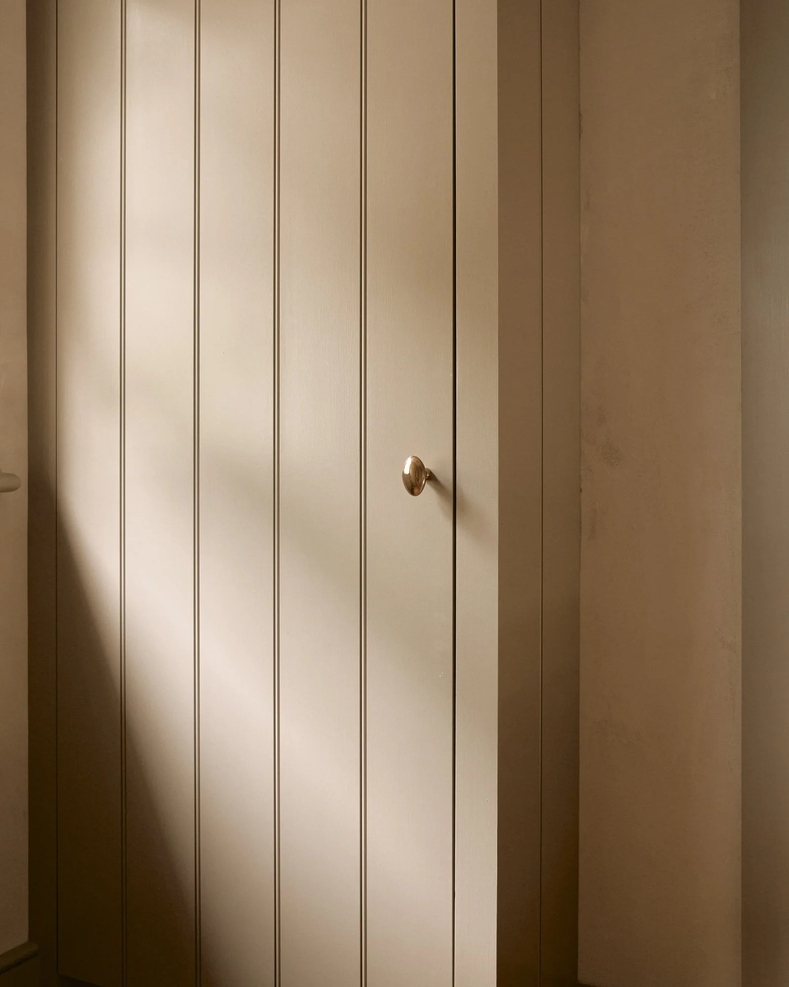 A beige paneled closet door with a round brass knob.