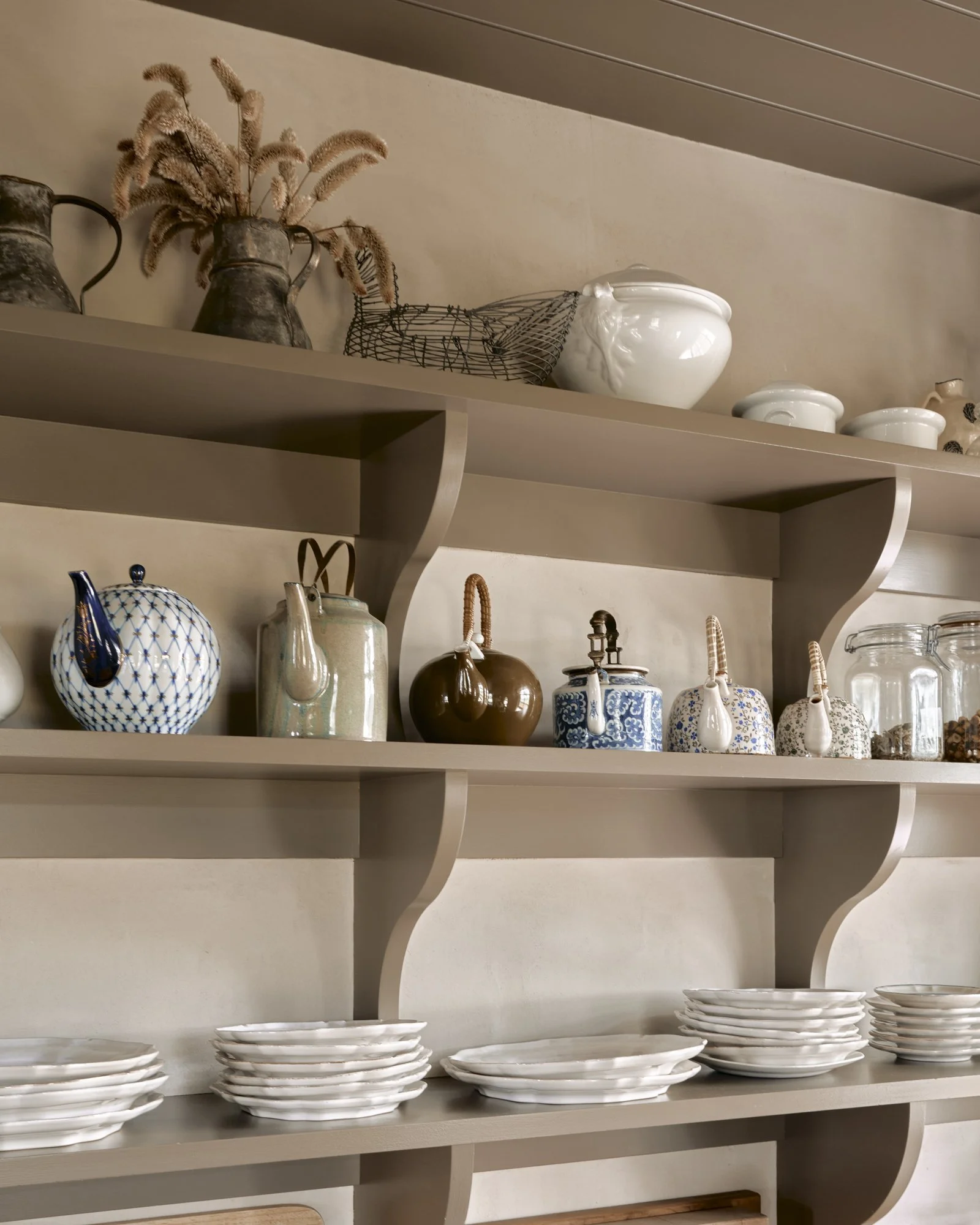Decorative kitchen shelves with tea pots, ceramics, glass jars, and stacked white plates.