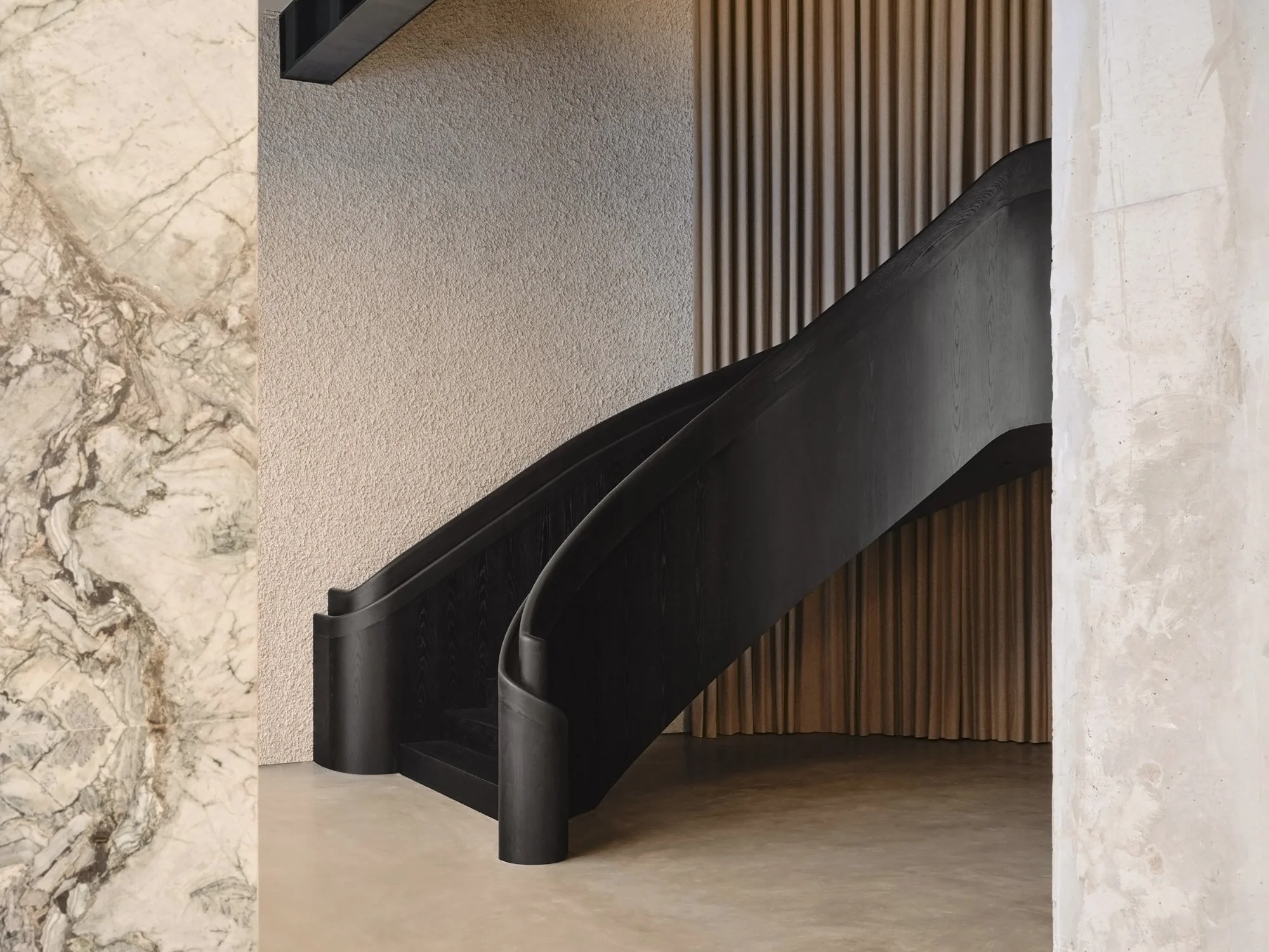 Saint Laurent flagship interior featuring a sculptural black staircase framed by marble and vertical wood paneling