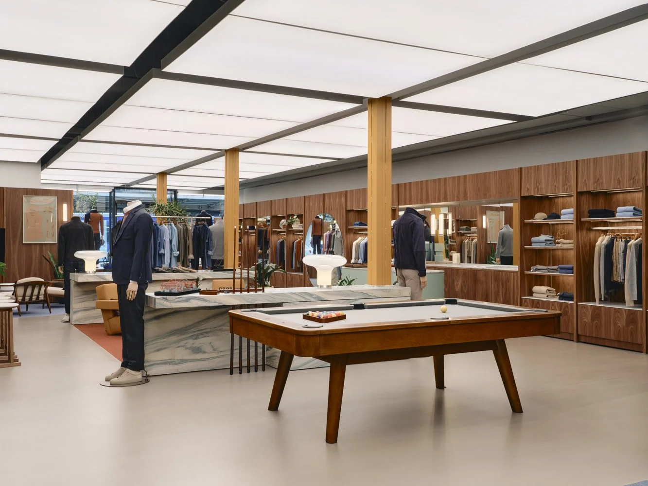 Interior of a modern clothing store with mannequins, clothing racks, a pool table, and wooden shelving units.