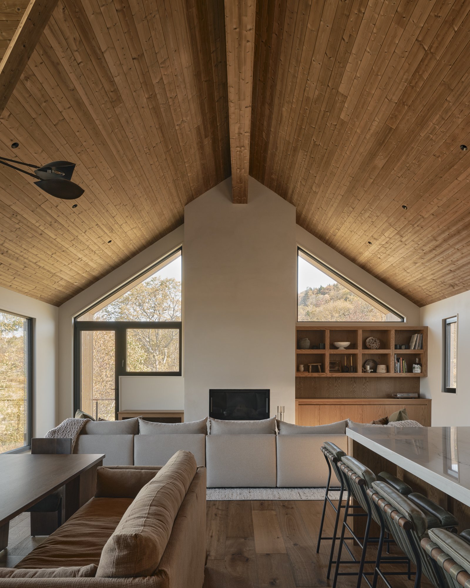 Living room with a vaulted wooden ceiling, large windows, white sectional sofa, and built-in wooden shelves.