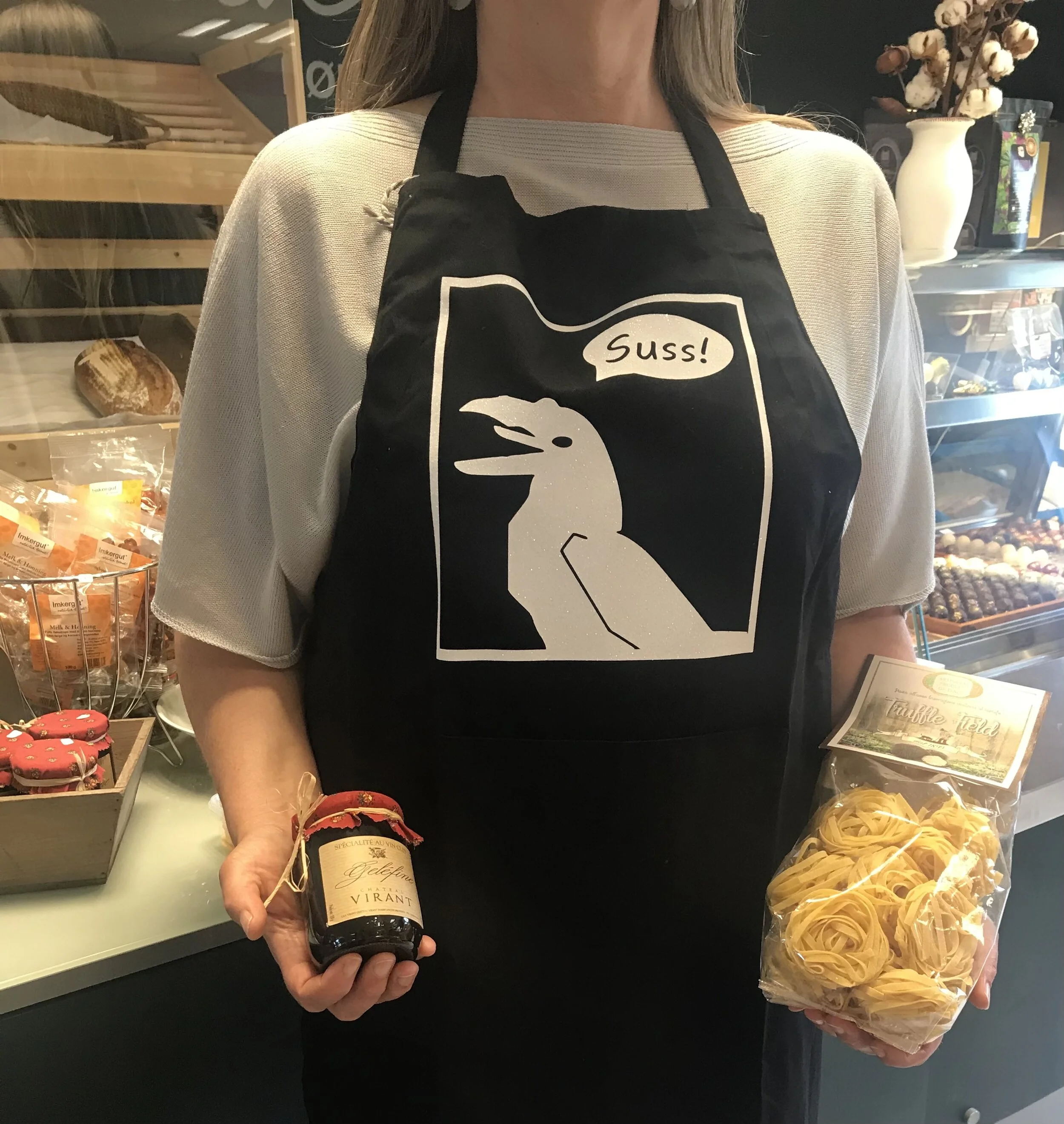 Forkle med trykk av kråka og  "Suss!" -  i sort bomull