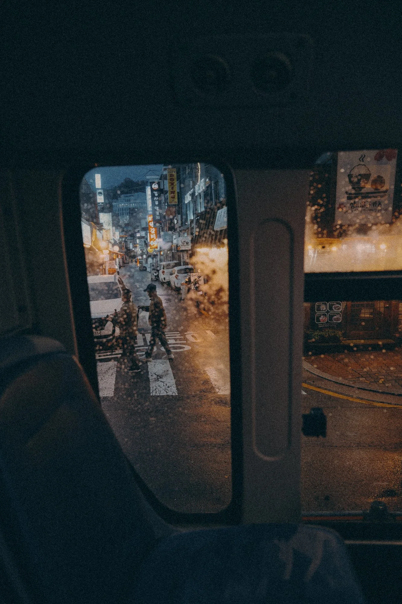 A Seoul street through a bus window on a rainy night.