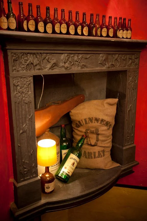 Trinity Irish Pub design - stone fireplace by Guiness designers with Jameson bottles inside and Guiness bottles on the mantlepiece