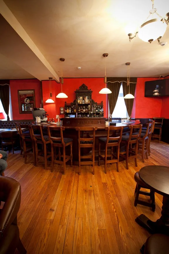Trinity Irish Pub Design - Interior view curved wooden bar and stools with red walls