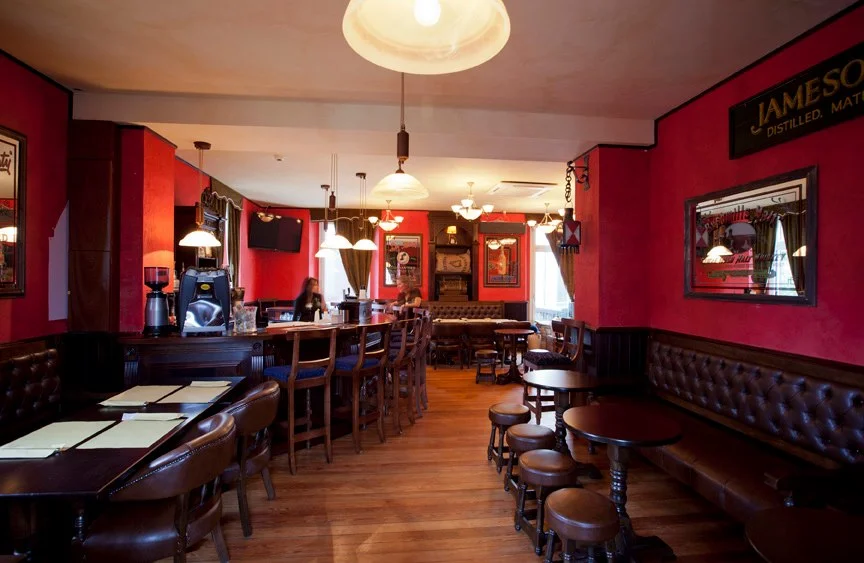 Trinity Irish Pub Design - interior view, low wooden tables and stools with leather upholstered sofas and red walls&nbsp;