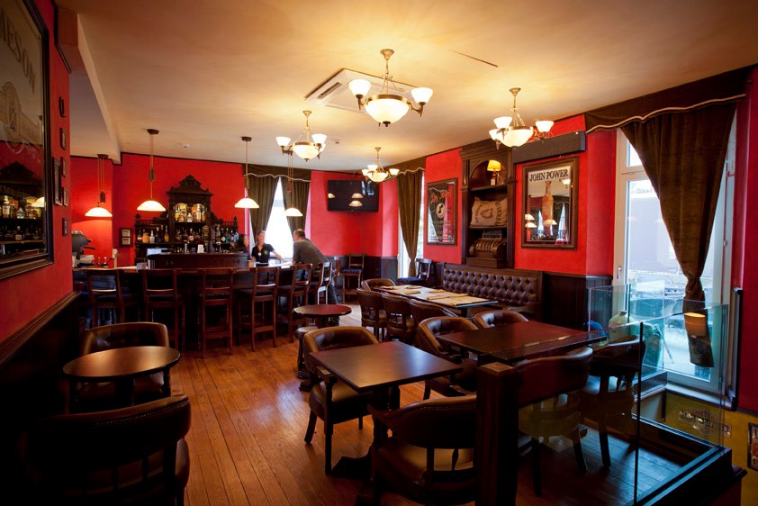Trinity Irish pub design - interior view dining area with low wooden square tables and chairs, red walls and heavy red velvet curtains
