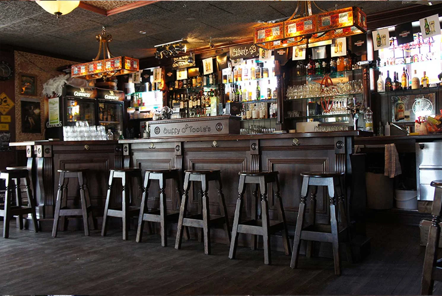 Duffy O'Toole's authentic Irish pub design - interior view of dark wood bar with 'Duffy O'Toole's' engraved into wood and high wooden stools lined up.&nbsp;