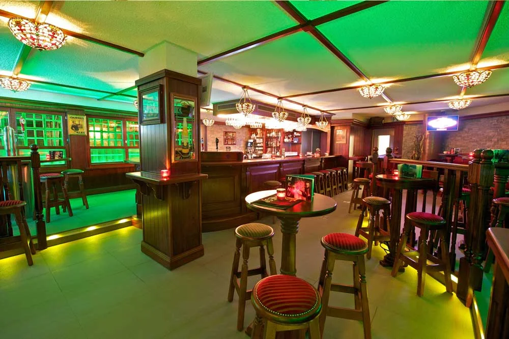 Papperla authentic Irish pub design - interior view of seating with green lighting, high wooden tables and wooden stools&nbsp;