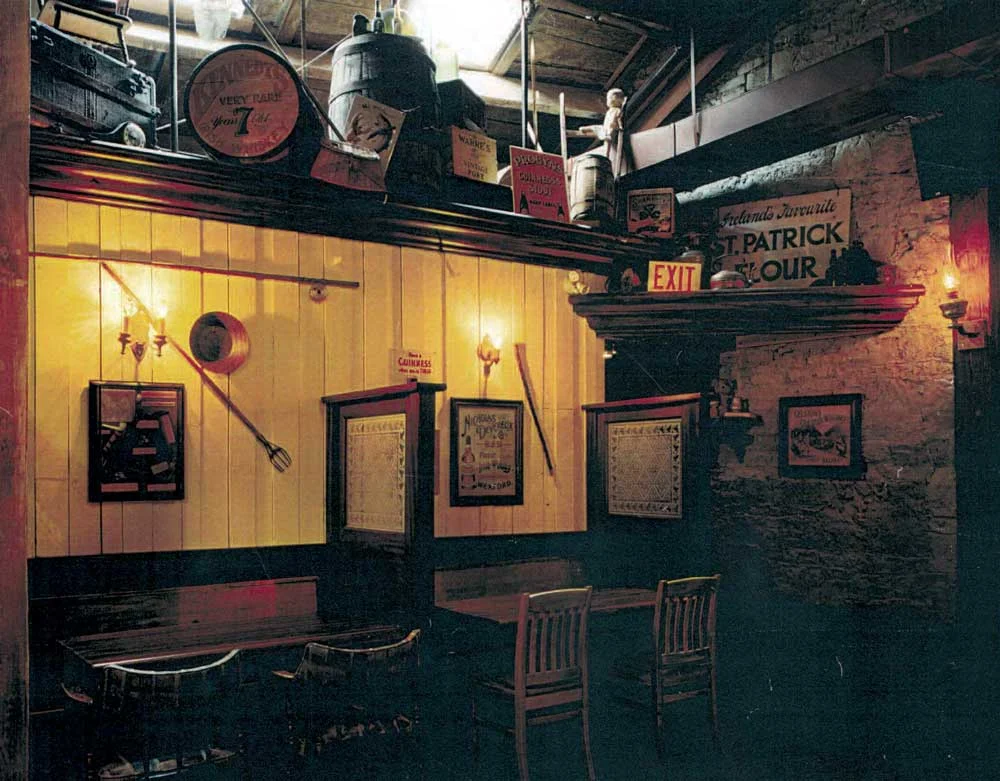 Country Cottage authentic Irish Pub Design - view of interior seating area with low wooden tables and chairs, soft yellow lighting and Irish adornments.