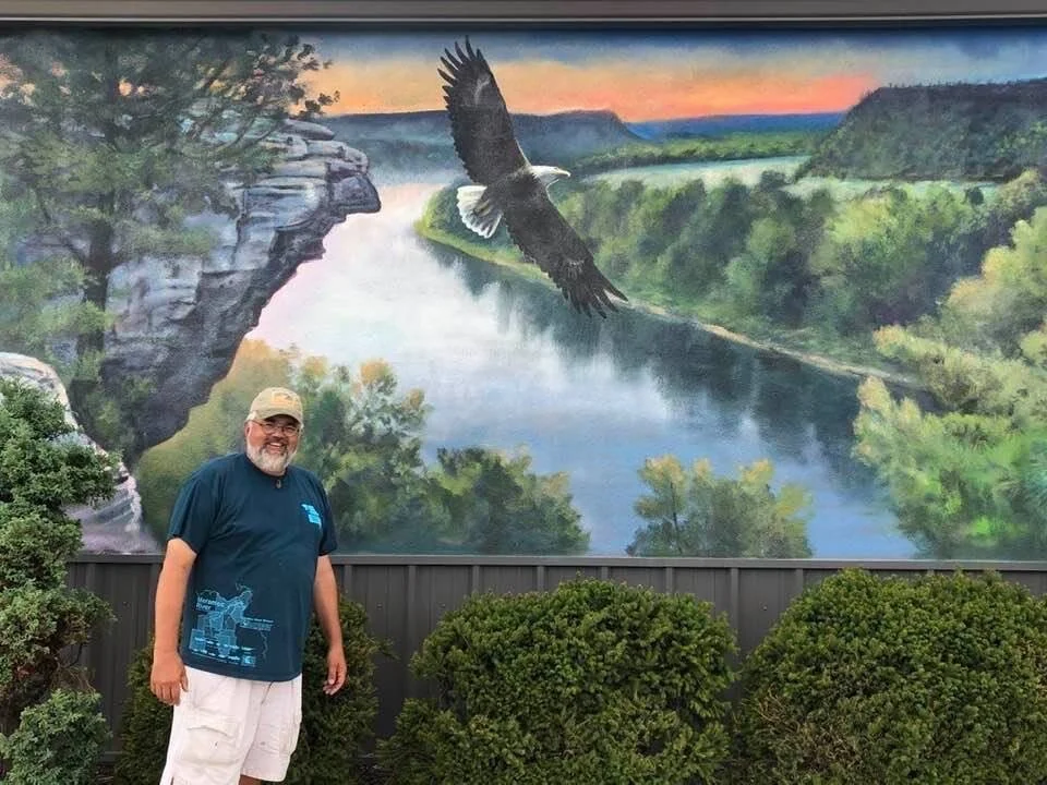 Duane hada poses with his mural at century 21 in mountain home arkansas