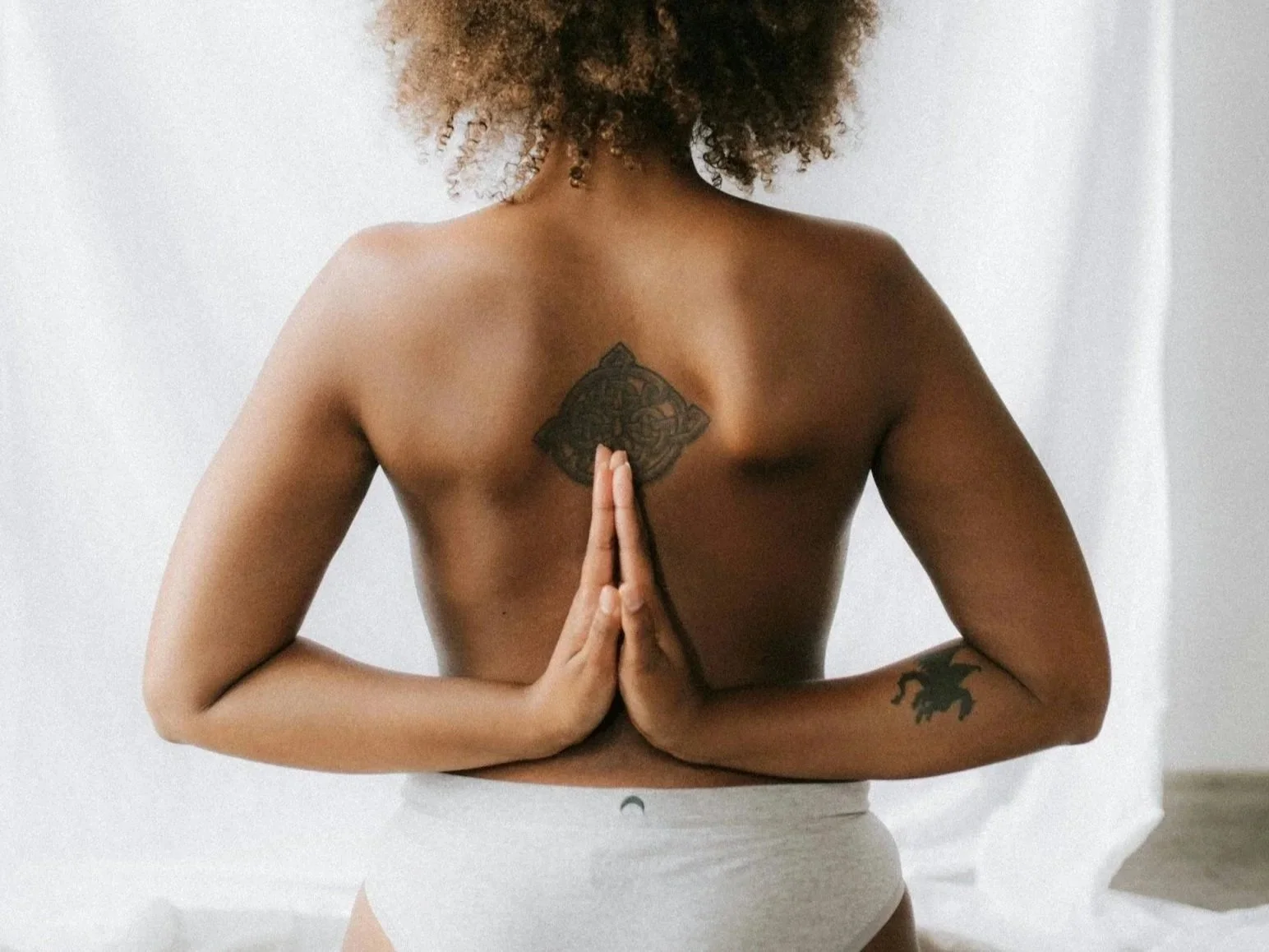 topless female seen from behind with hands behind back in namaste shape depicting suppleness of limb and smoothness of skin