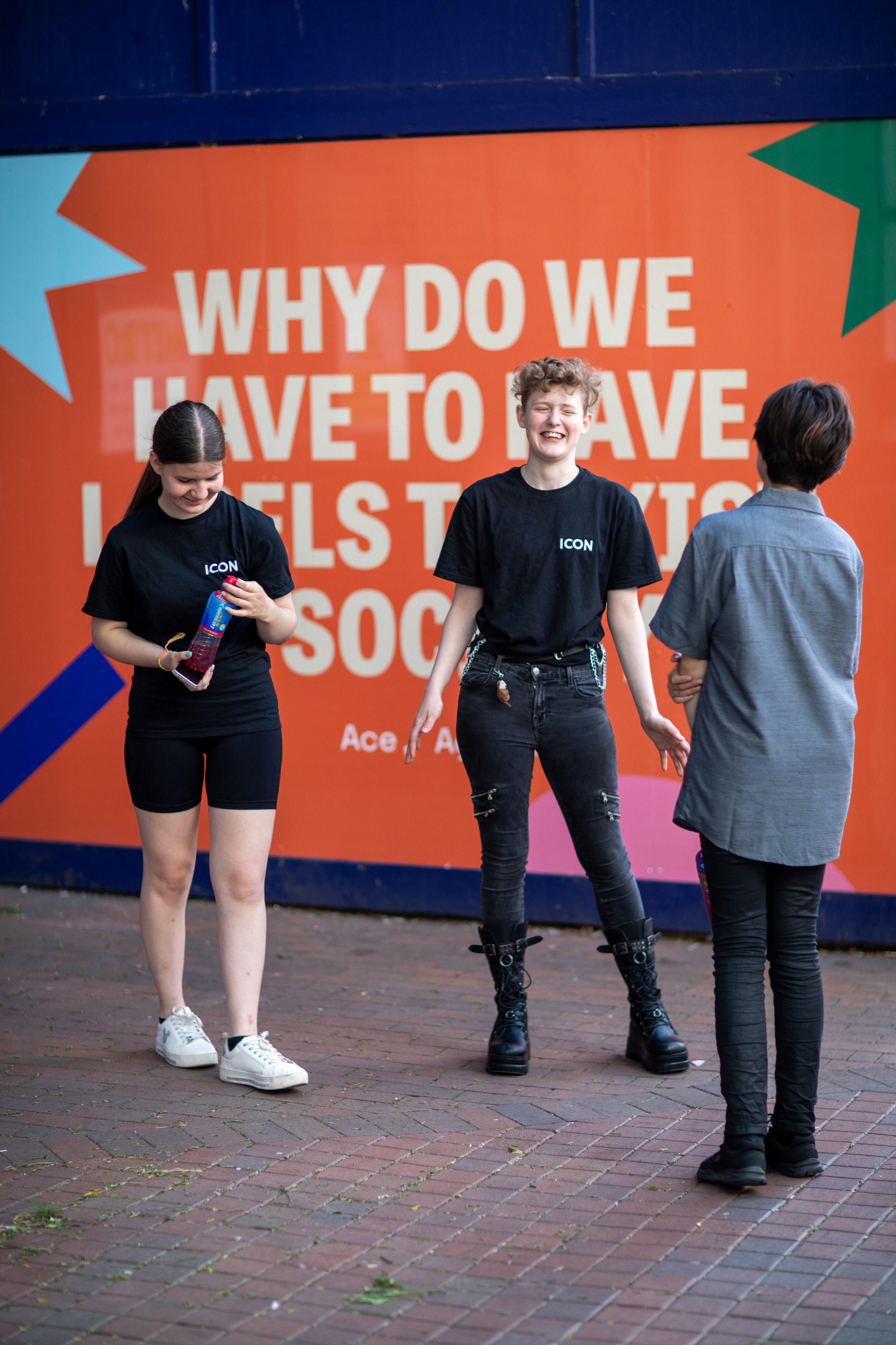 Teenagers hang out on the street happily. Smiling in front of a huge artwork featuring the quote of a fellow young person.