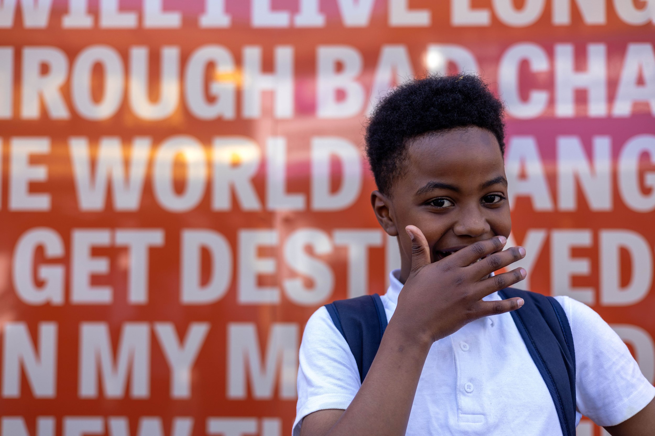 A child smiles, covering their mouth in joy. Behind them, colourful artworks are out of focus.