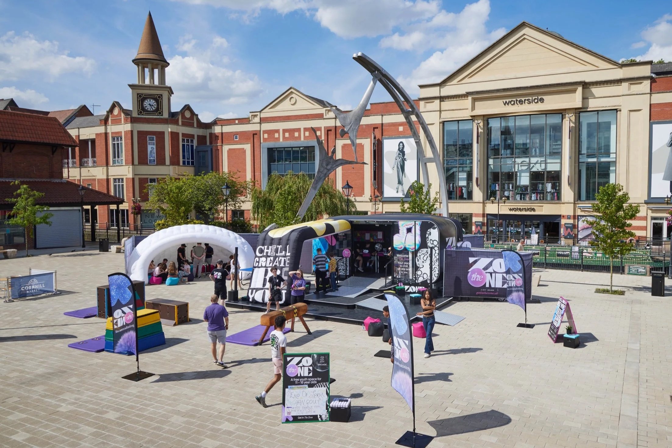 The Zone stands in Lincoln city square on a sunny day. A colourful trailer with various inflatable structures.