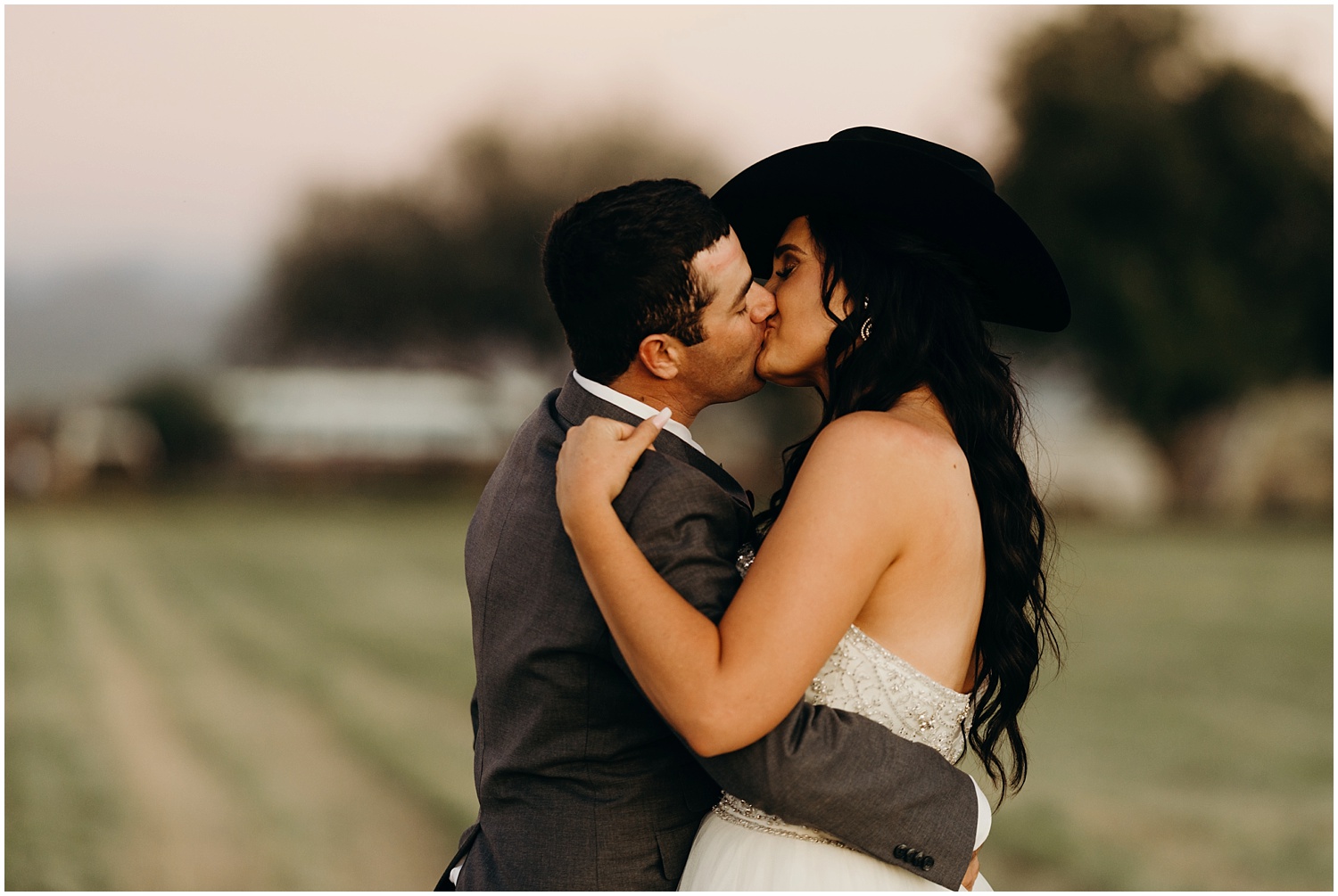 Groom puts cowboy hat on his bride and kisses her.