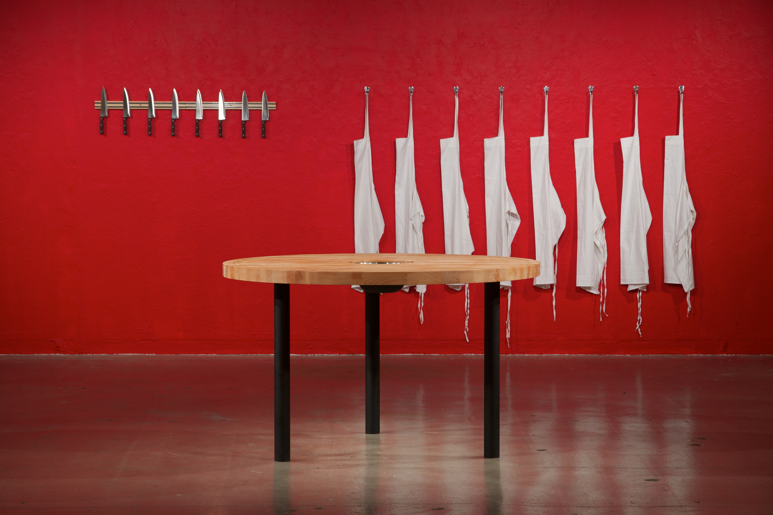   The Pleasures of the Table  2012 maple butcherblock, mixing bowl, metal, 8 chefs knives, magnetic knife rack, 8 aprons, metal hooks Dimensions variable 