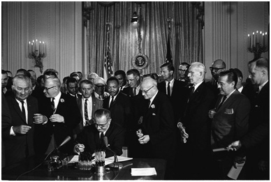 Dr. Martin Luther King Jr. stands behind President Johnson as he signs the landmark Civil Rights Act of 1964. – Photo: Wikipedia, Cecil Stoughton