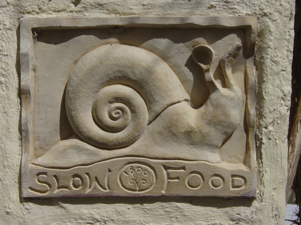 The snail was chosen to be the patron and symbol of the slow food movement. The plaque here was found on a wall outside a restaurant in Santorini, Italy .