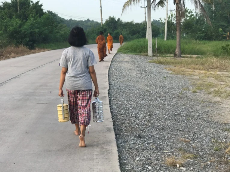 A young Thai girl follows three novice monks in the collection of the morning alms, in which they accept donations of food and drink to the temple from residents throughout the village of Chonburi. – Photo: KP