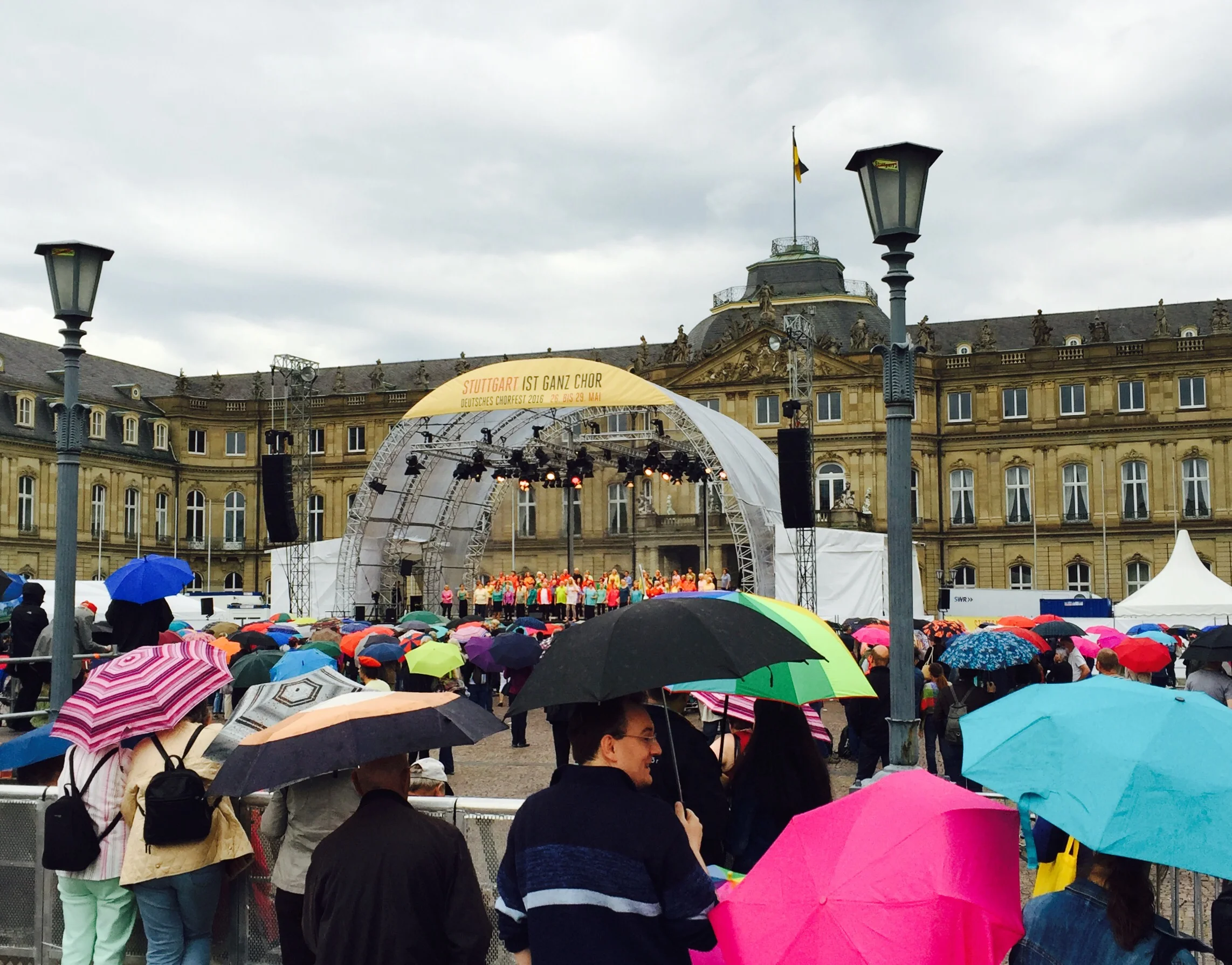 A large crowd listens to choral music standing in the rain.