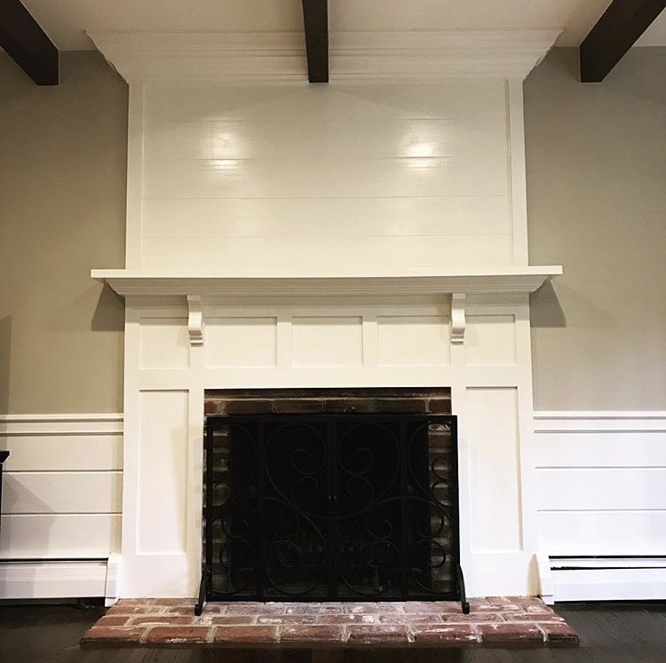  The finished product has a flat panel design for the lower half, and custom horizontal wainscot paneling on the upper half to echo the existing horizontal paneling on either side of the fireplace. Custom corbels support the new mantle, and the top i