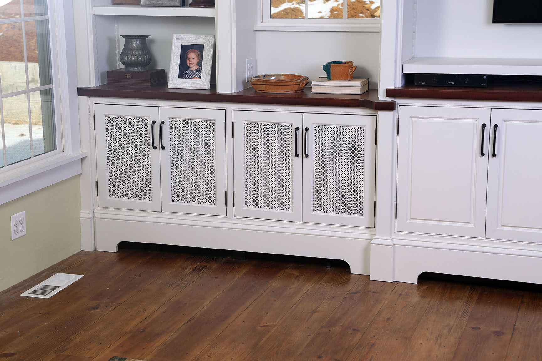  The left-side doors conceal an existing radiator behind a false cabinet front that swings open to provide access when needed. The arched baseboard lets air in to the radiator, and the open mesh doors allow heat to flow out to the room. 