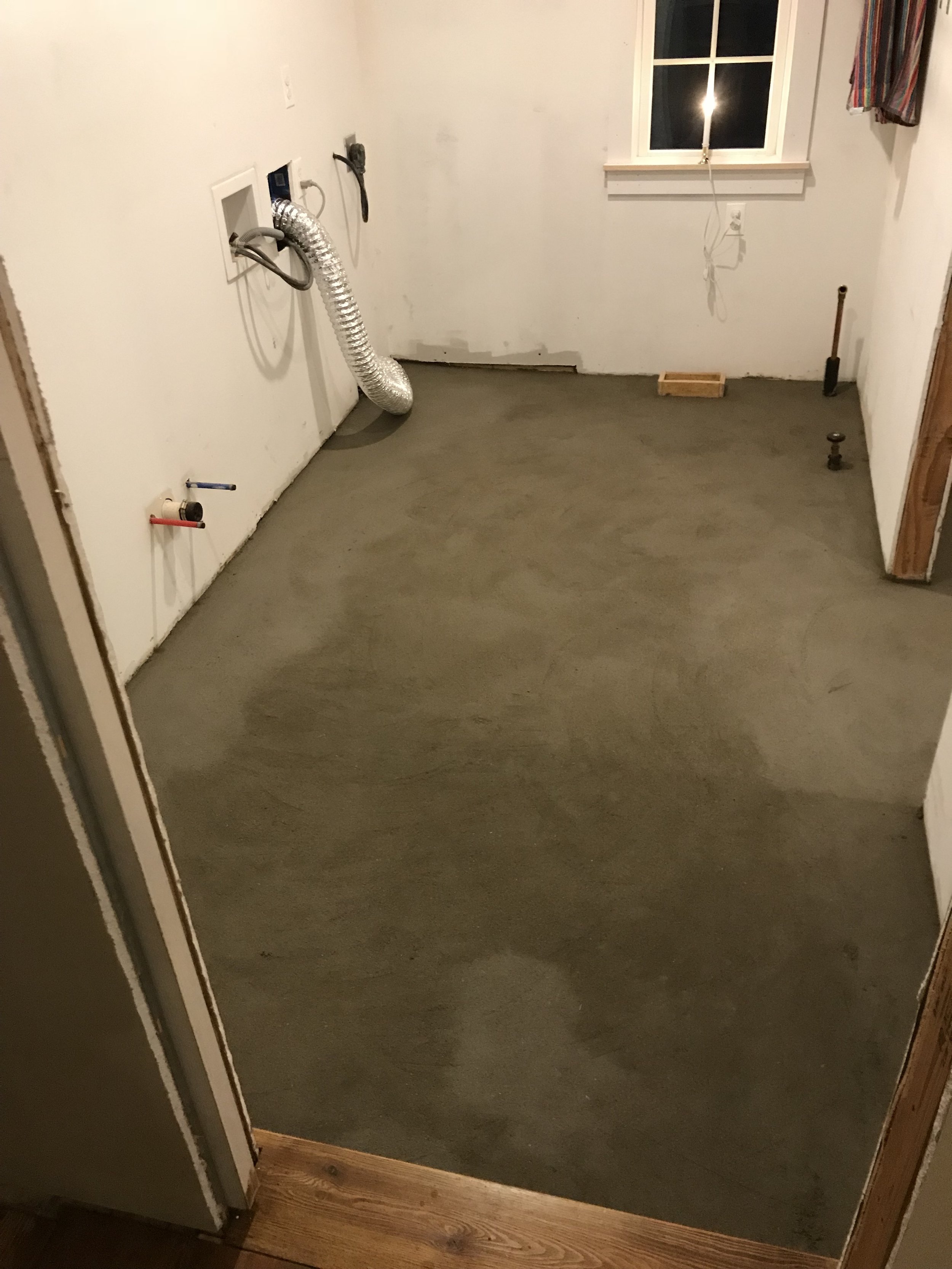  A base layer of mortar, the wet bed, is installed over the wire mesh, and the whole thing is pitched towards a drain in the neighboring mudroom. This is to drain water out quickly if the washing machine ever springs a leak.  