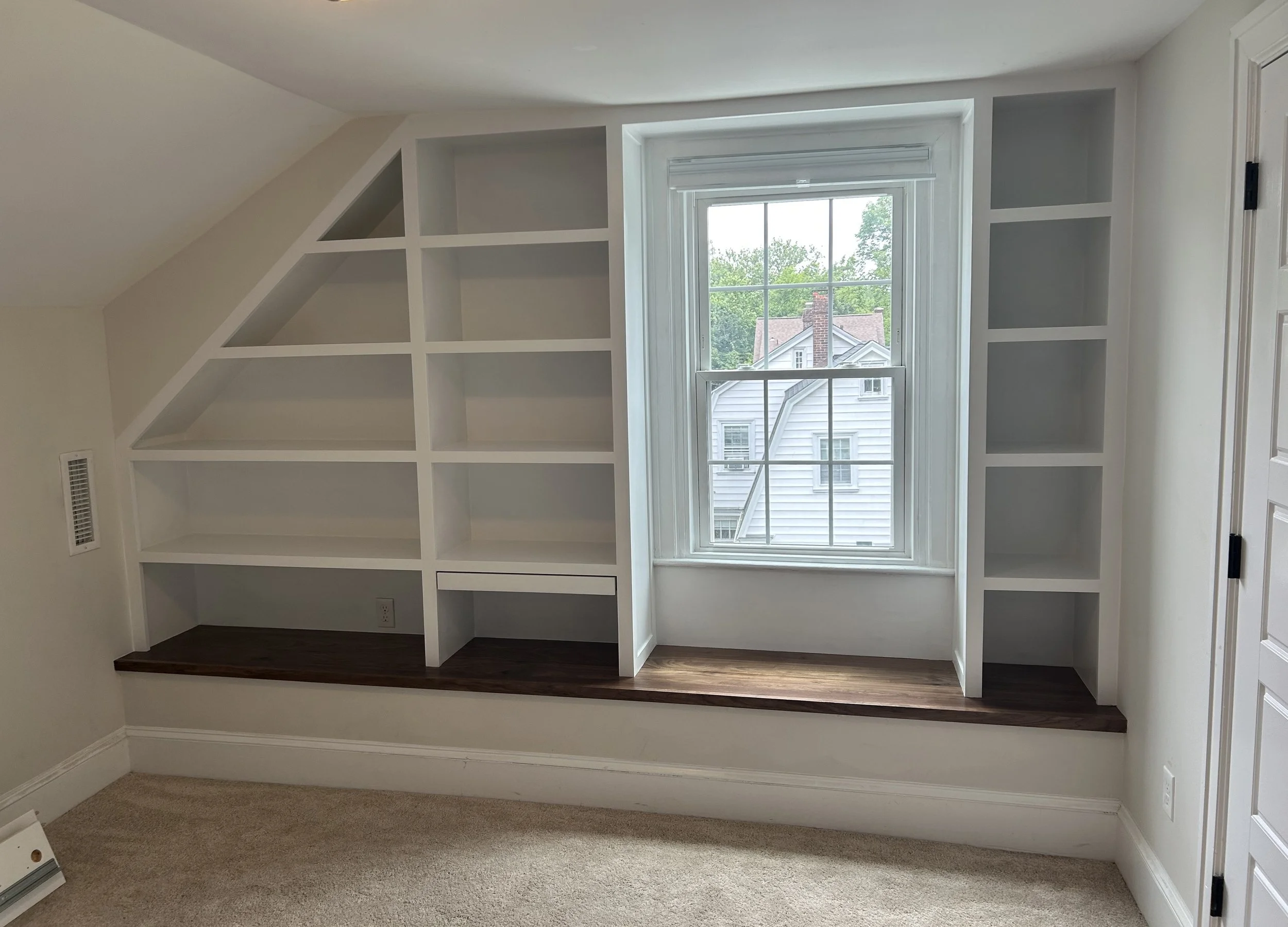  This angled bookshelf unit sits on top of an existing HVAC soffit that was in the room. Instead of trying to reroute all the ducts inside, I turned it into a window seat with a beautiful black walnut top, saving both time and money.  Access was so t