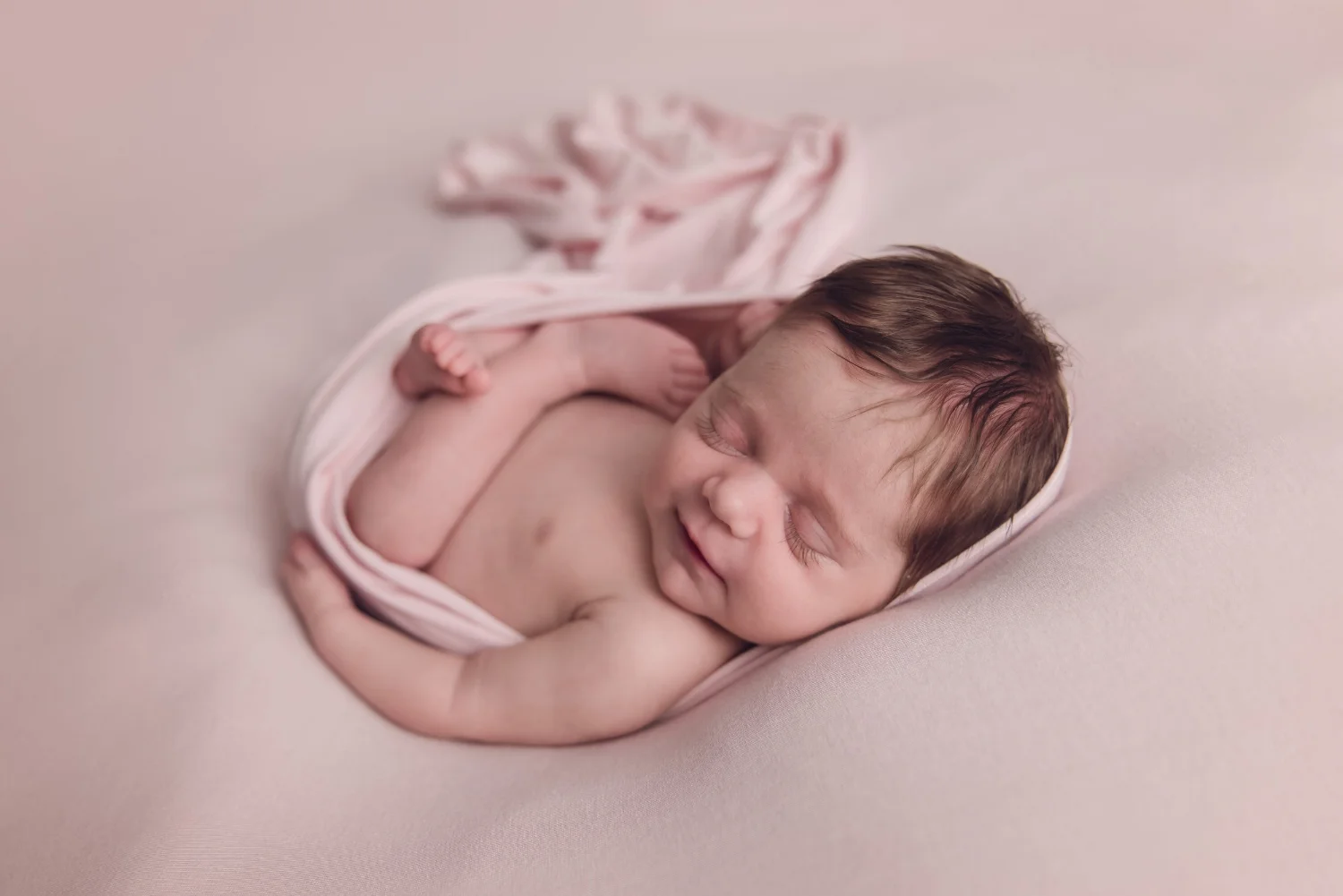 Baby girl curls up on pink fabric for studio newborn session. #bestpeorianewbornphotographer