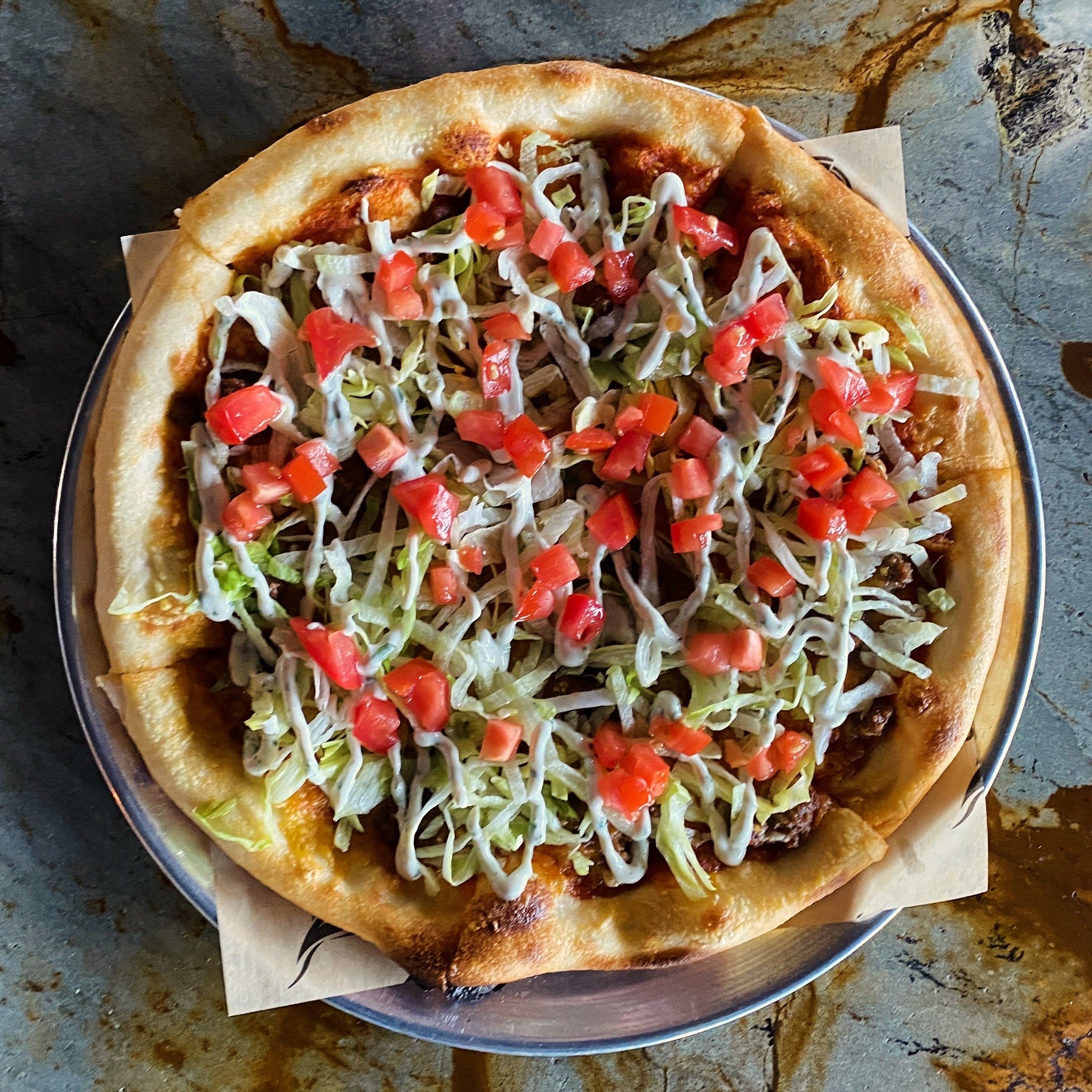 Celebrate Cinco de Mayo with this month&rsquo;s feature pizza! Taco sauce, seasoned ground beef, red onion &amp; cheddar jack, then lettuce, tomato &amp; cilantro lime crema after the bake. Make the celebration more festive with our delicious margari