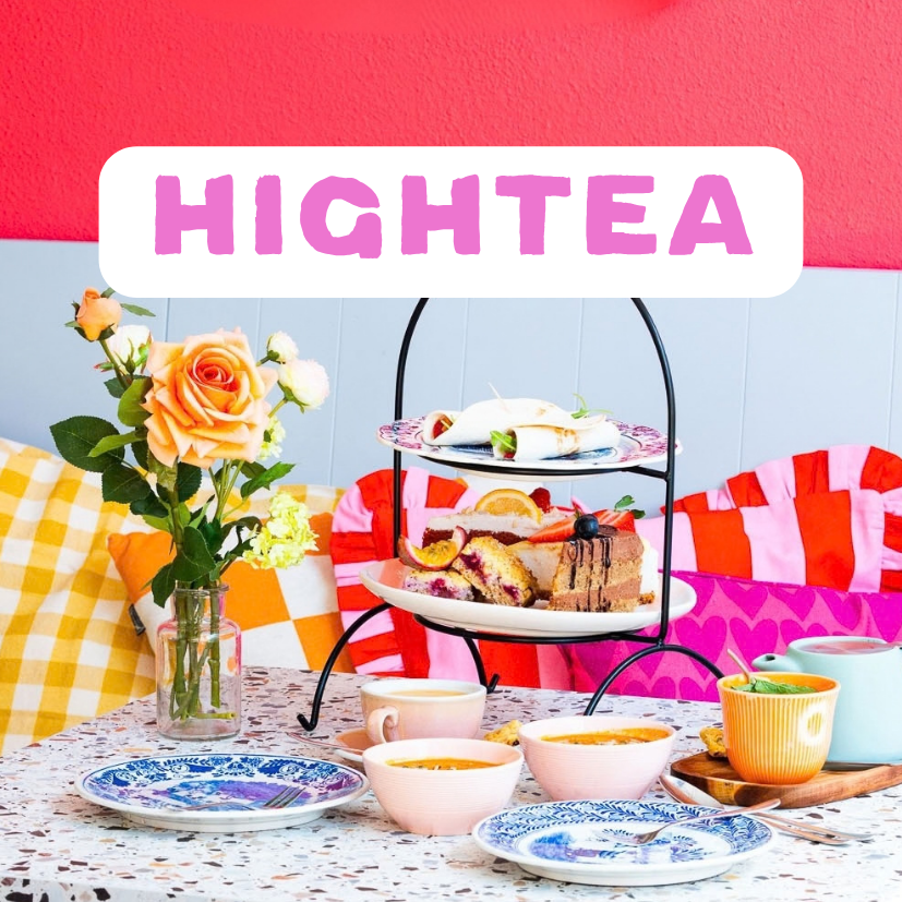 Een etagère met verschillende soorten taart en snoepjes, een vaas met oranje en witte rozen, en een tafel met koppen thee en serveerschaal met soep, op een kleurrijk ingekleed achtergrond. Een High Tea bij ETN in Enschede.