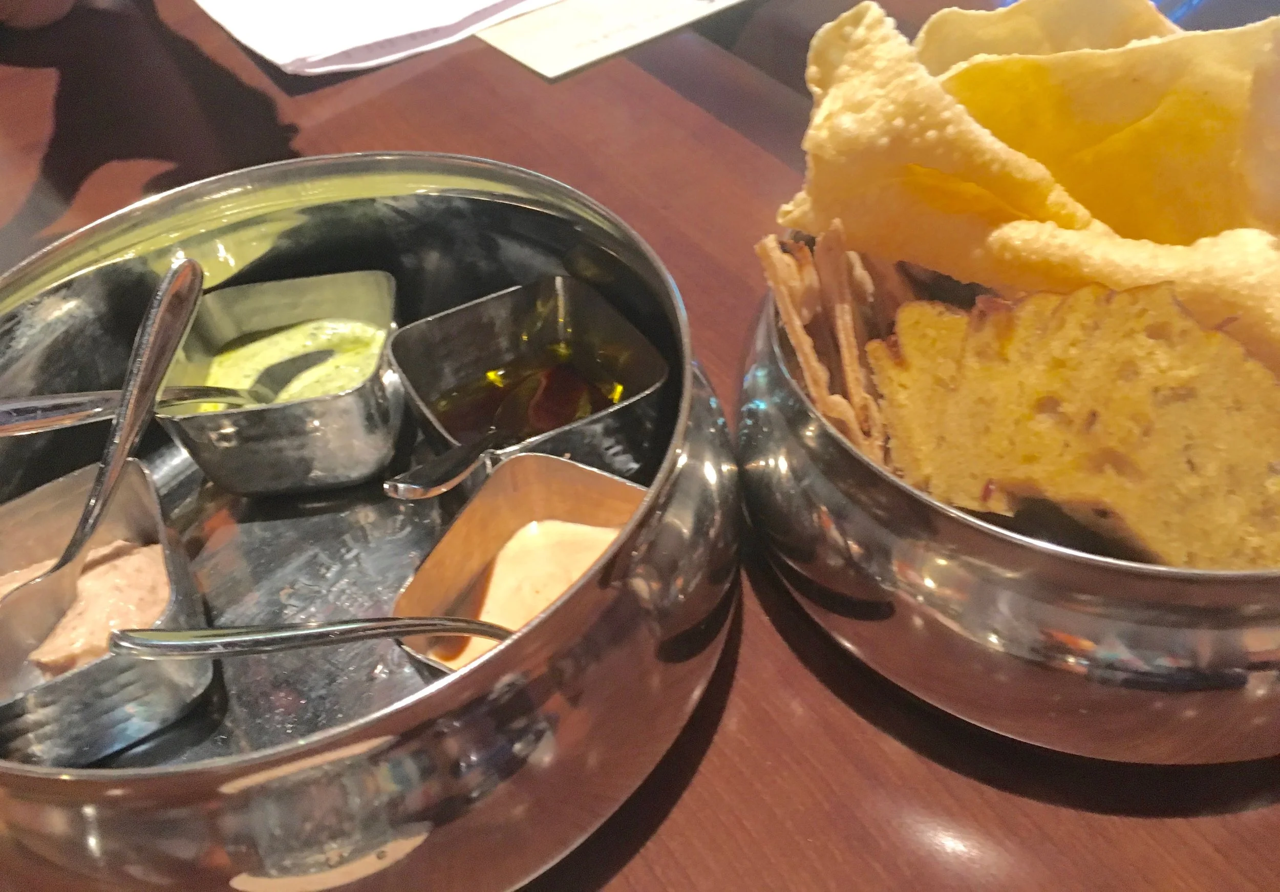 Kind of a chip-and-dip basket served in a "tiffin" lunchbox-style container. You see pappardam (lentil crackers) and roti (bread) with pomegranate olive oil, harissa yogurt, black-eyed pea hummus, and zhough yogurt at Tiffins