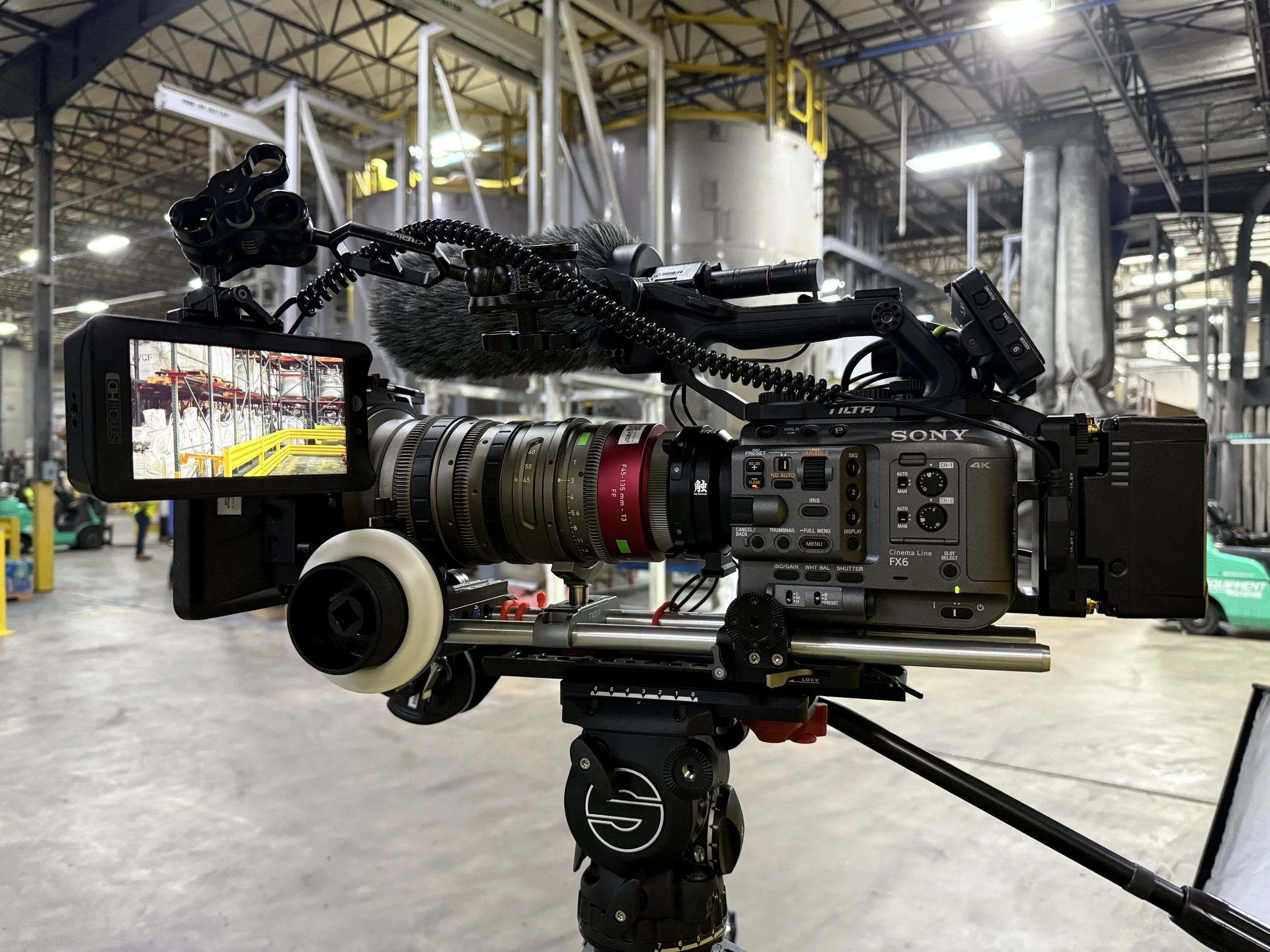 Professional video camera with microphone mounted on tripod in an industrial warehouse setting.