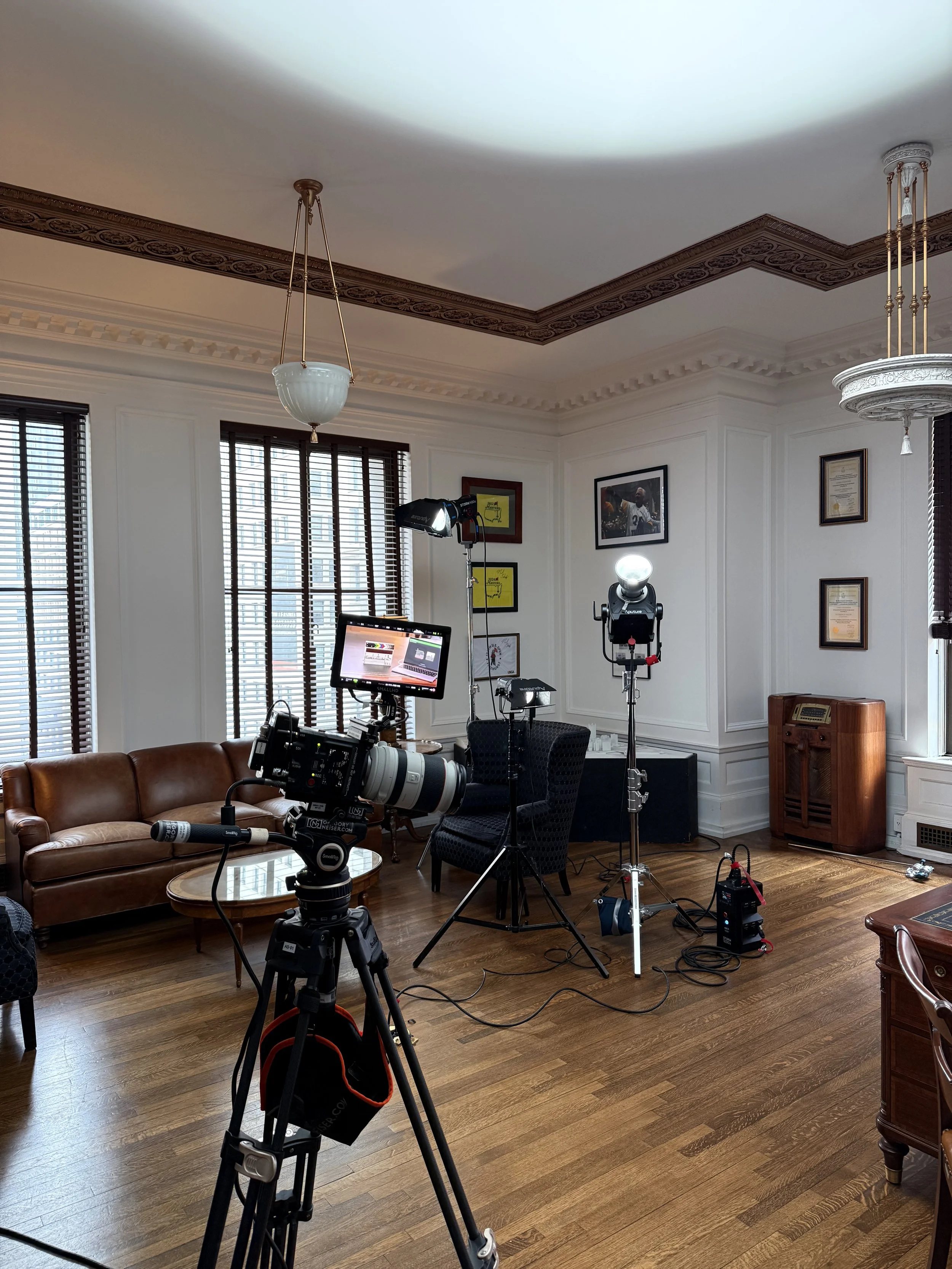 A room set up for video recording or filming with cameras, lights, a sofa, and wall decorations.