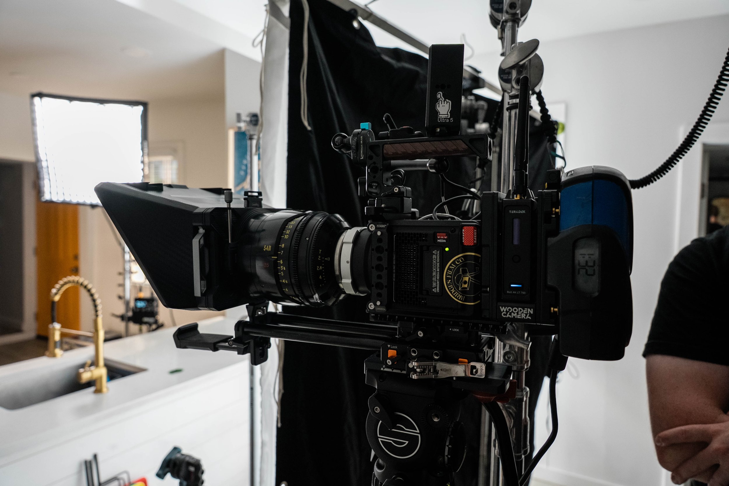 Close-up of a professional video camera mounted on a stabilizer, set up for filming in a room with a sink and faucet in the background.