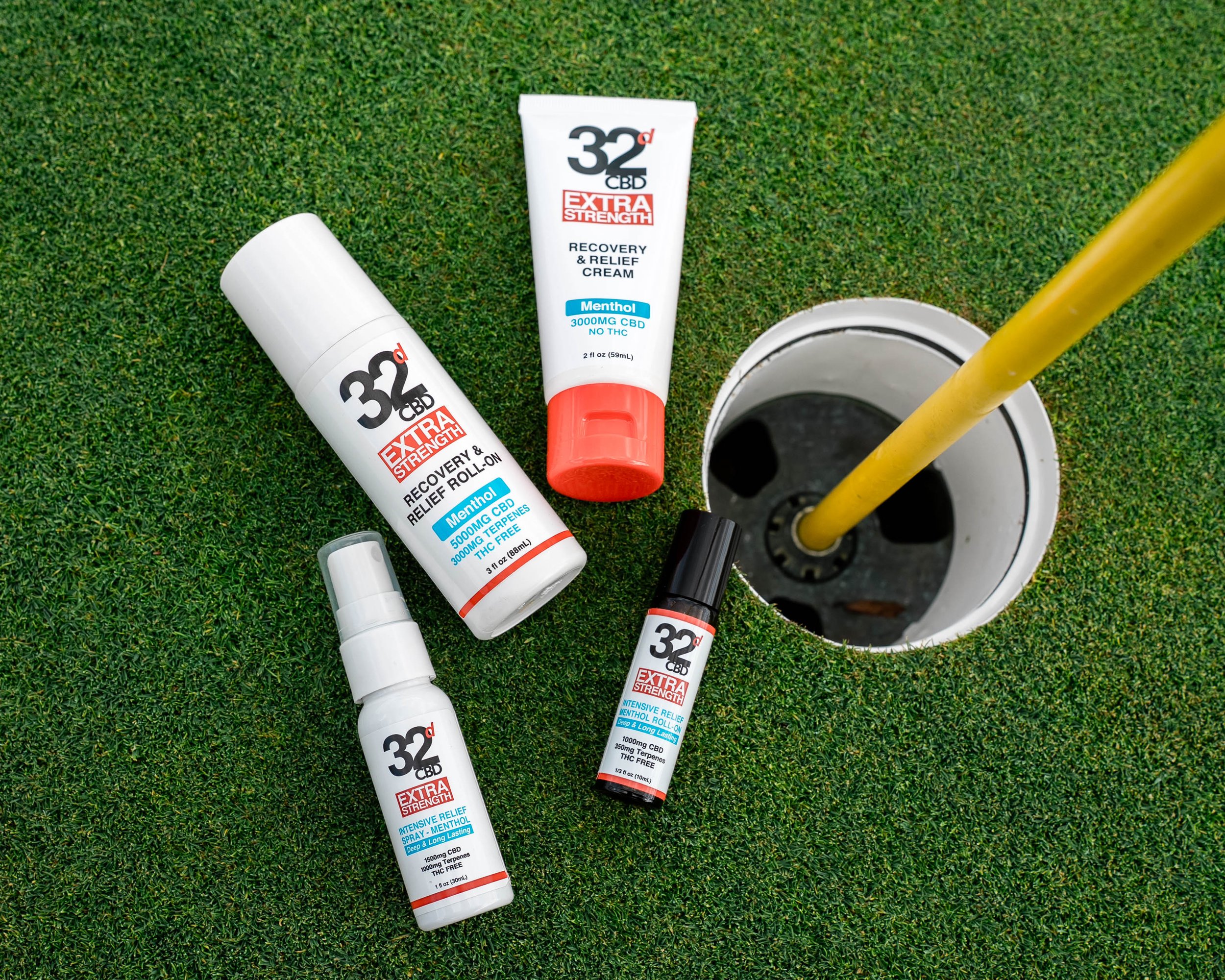 Golf green with a hole and yellow flagstick, surrounded by five CBD relief and recovery products.