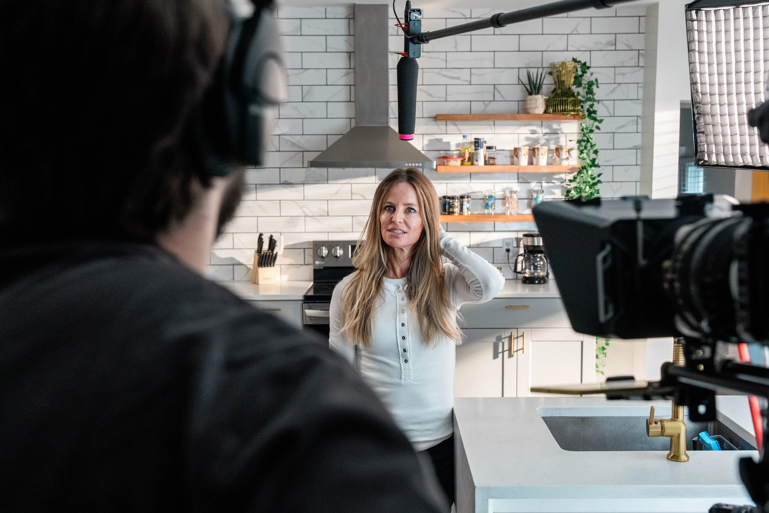 Woman being filmed in a kitchen for a video or interview, with filming equipment and camera visible in the foreground.