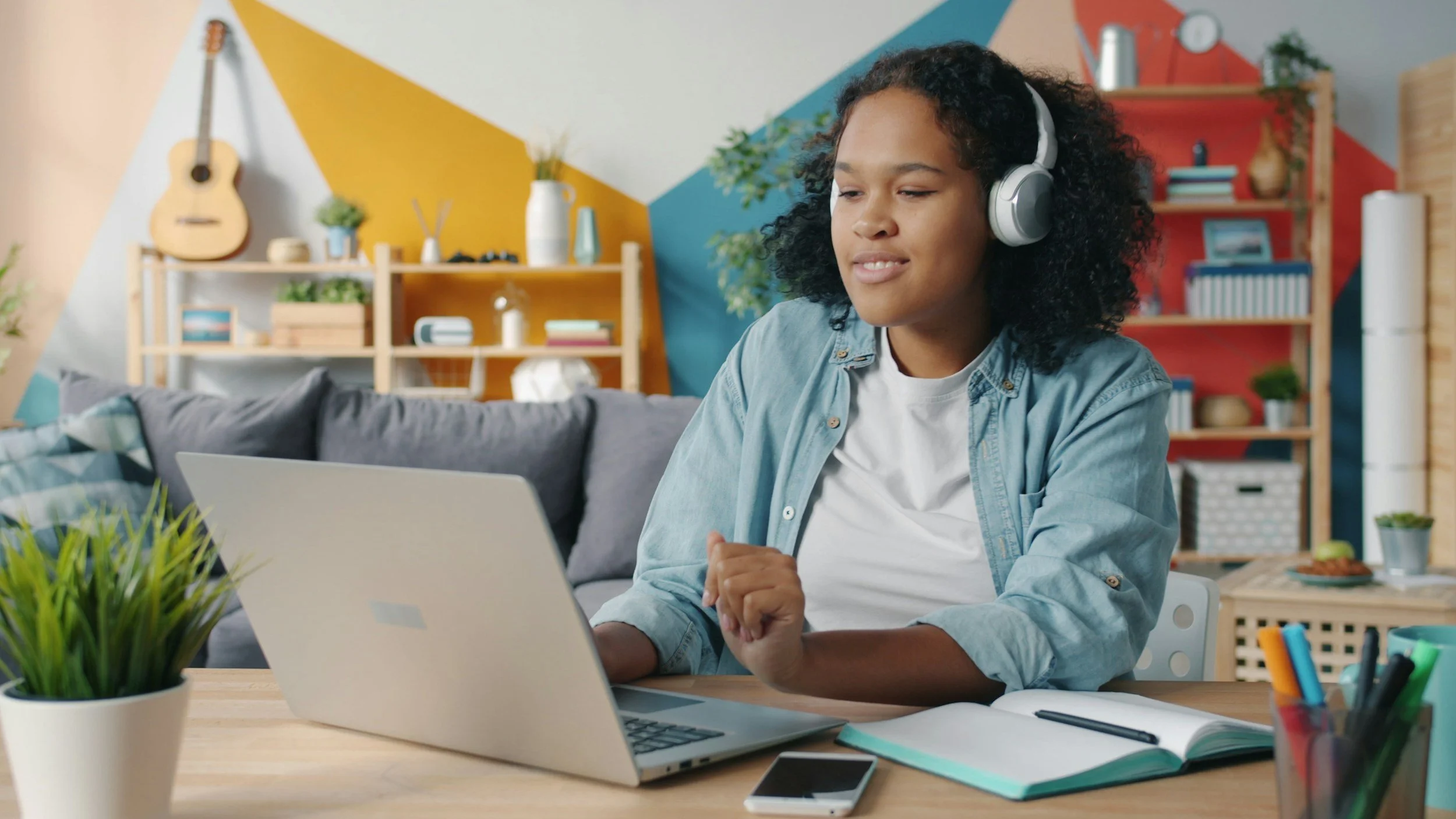a smiling teen wearing headphones works at a laptop