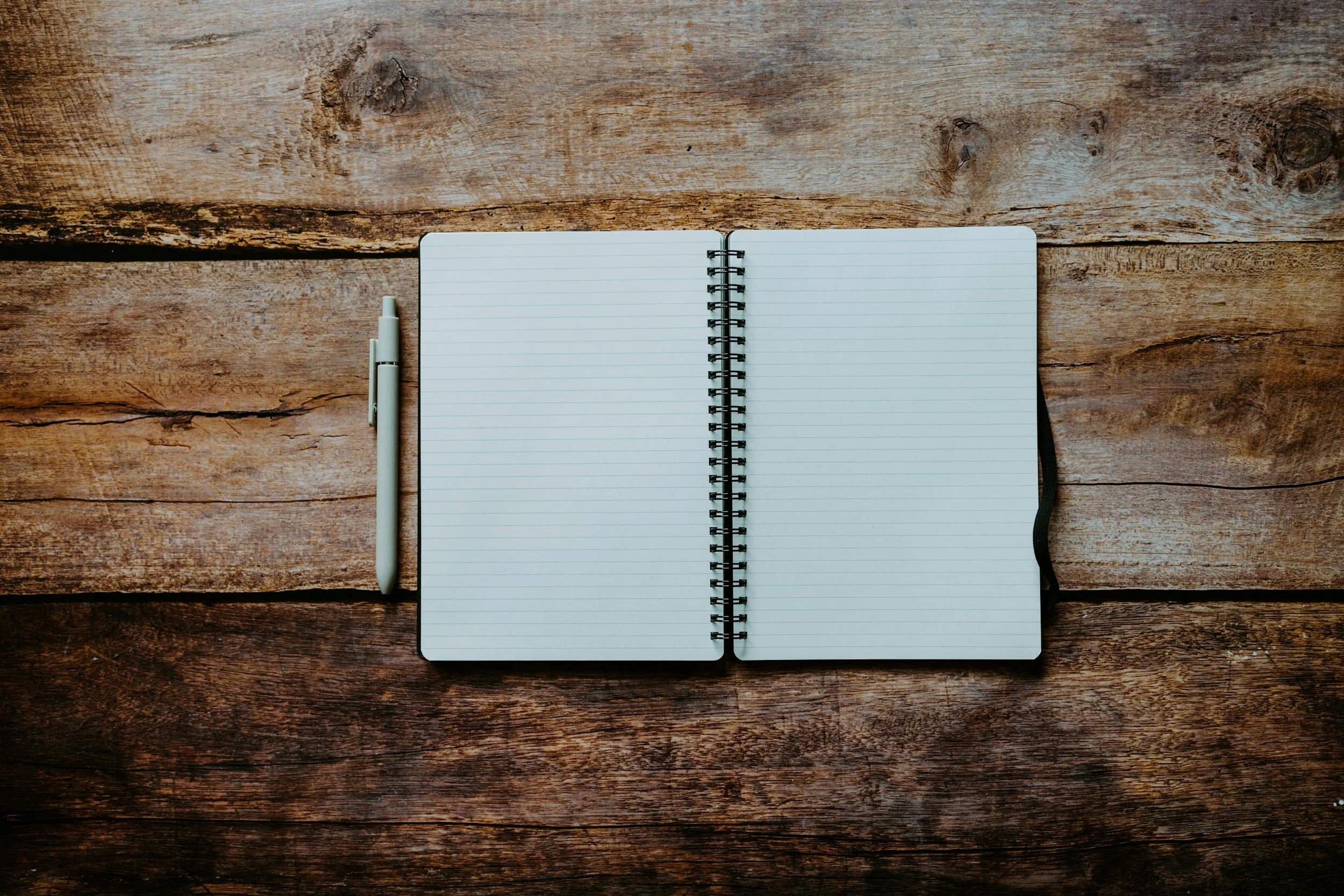 A blank, lined notebook lies open. A pen sits to the left of the notebook