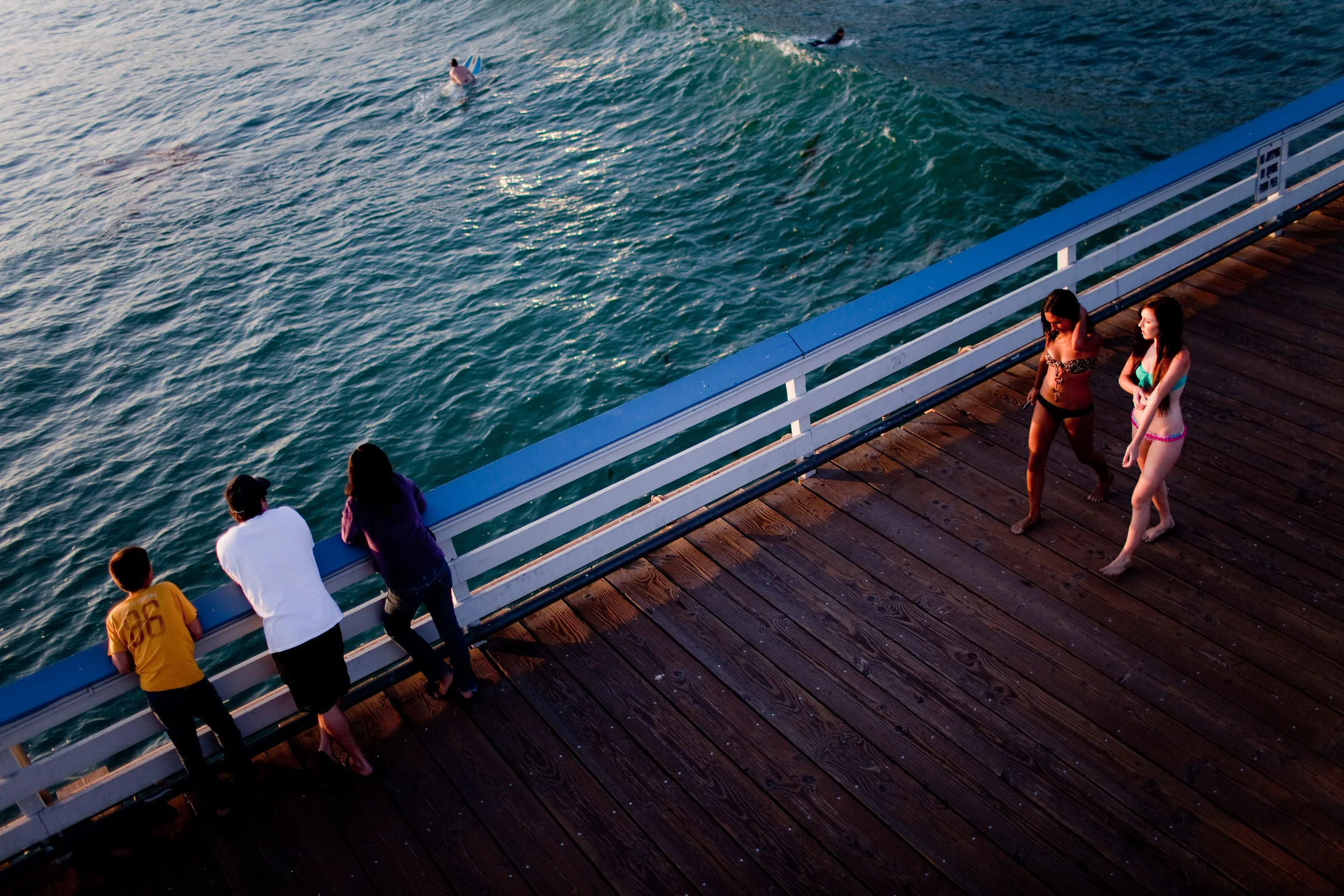 Two girls walk down the pier while a family watches the surfers in the water below in San Clemente, California. Surfing is a major attraction in San Clemente.