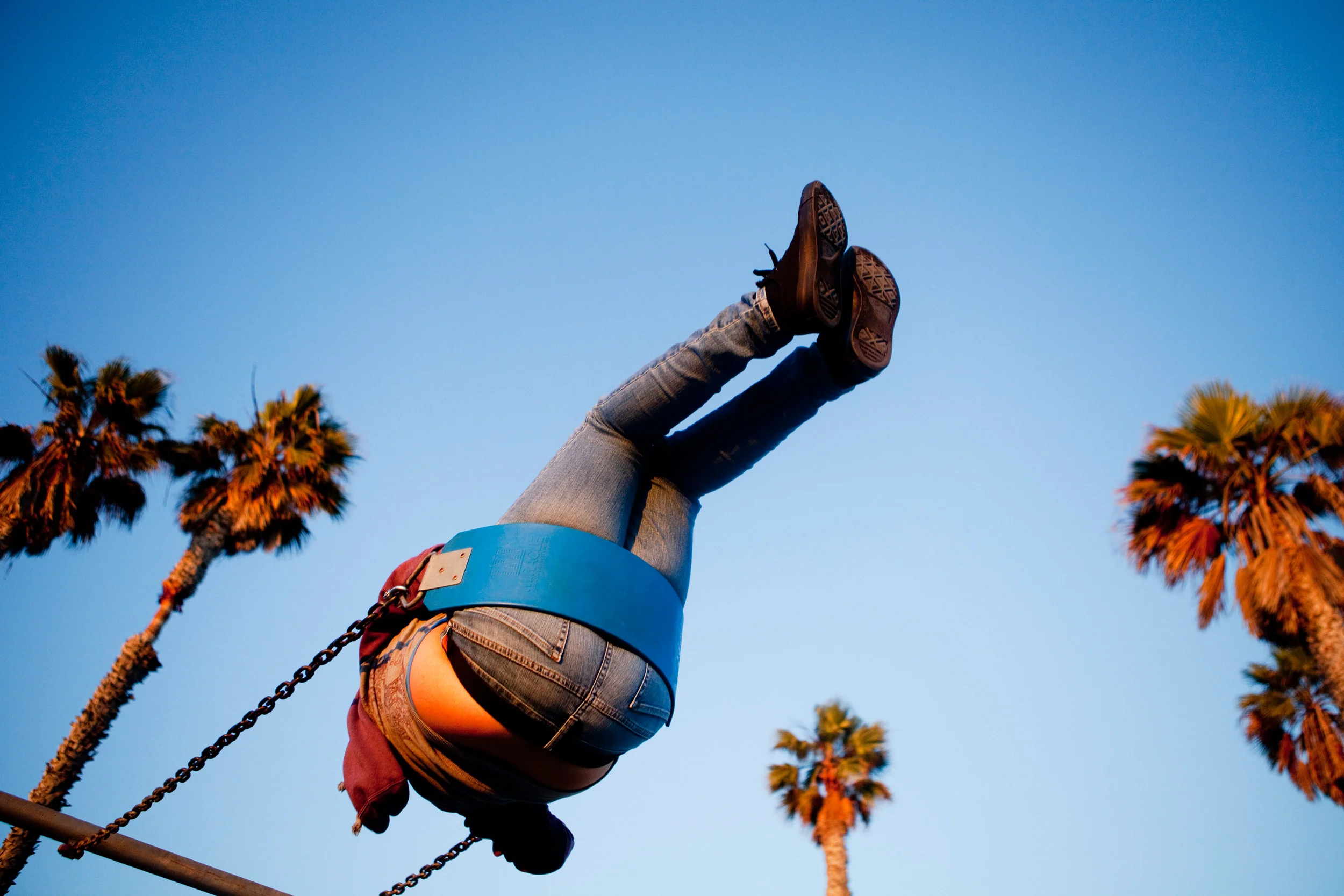 Lina Downey rises to the top of her swing and is surrounded by palm trees on the swing set near the pier in San Clemente, California.