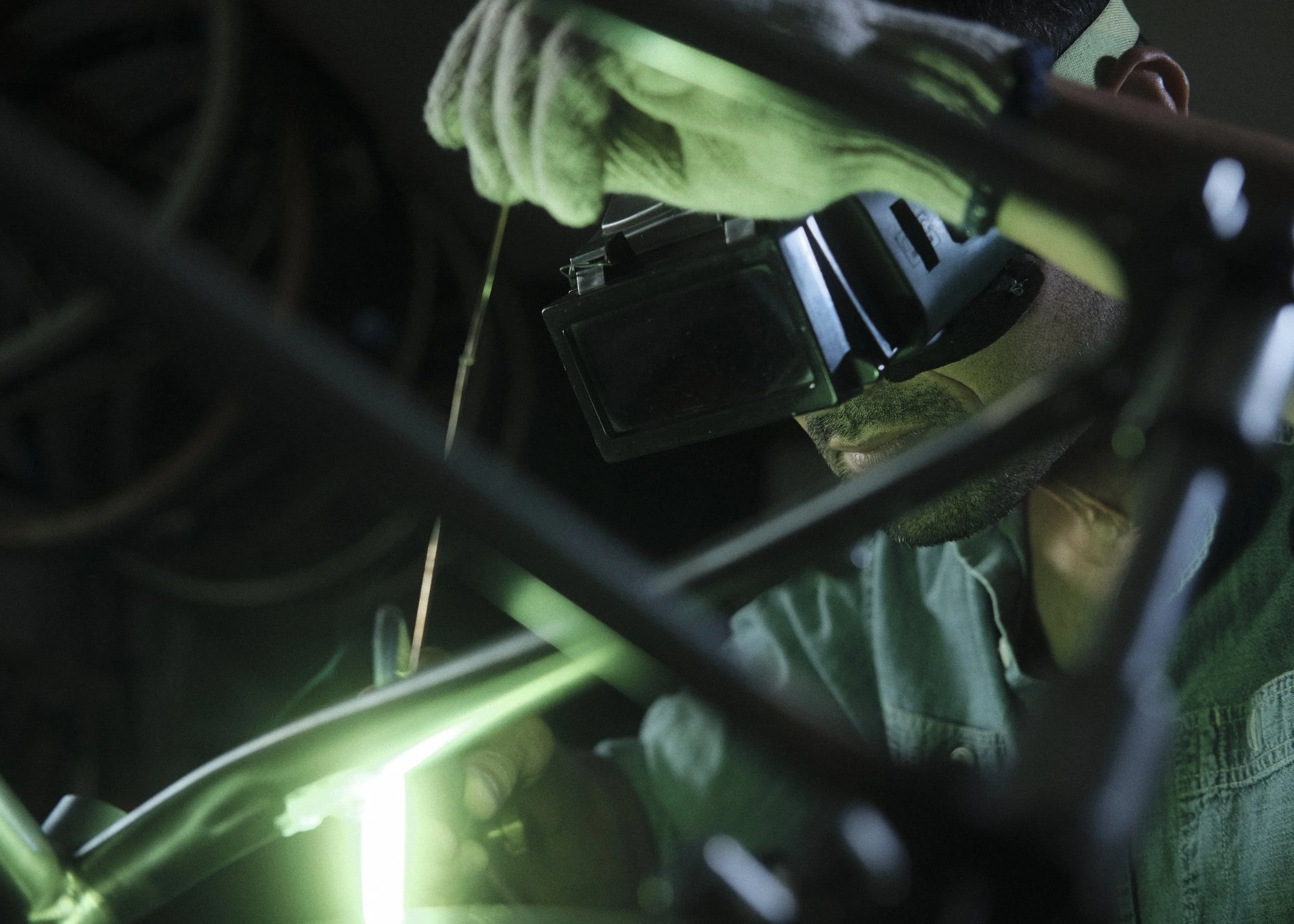 A person wearing gloves and safety glasses working with welding equipment, with sparks and green light visible.