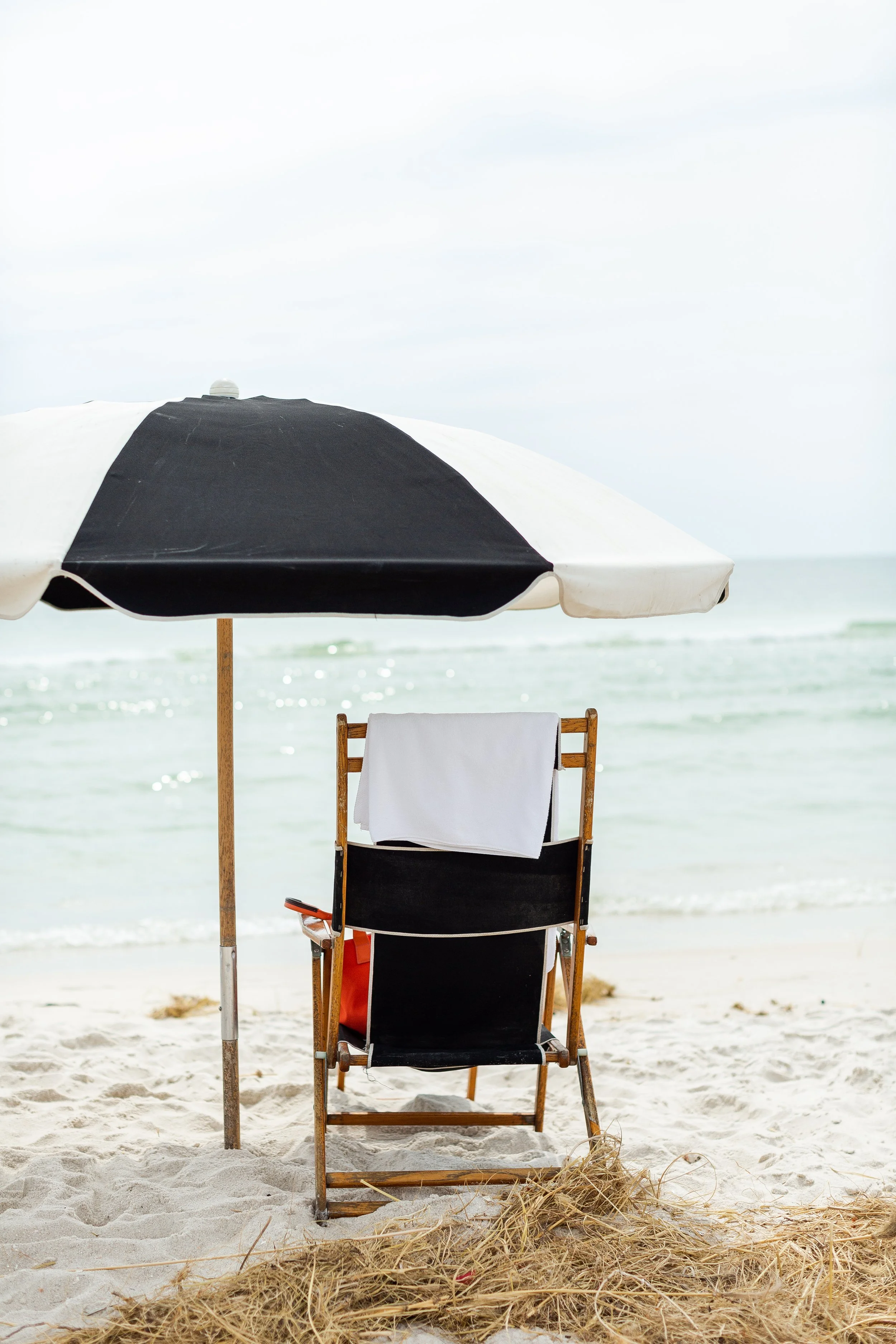 Beach scene with a black and white umbrella, a black beach chair with a white towel, on sandy shore near the ocean.