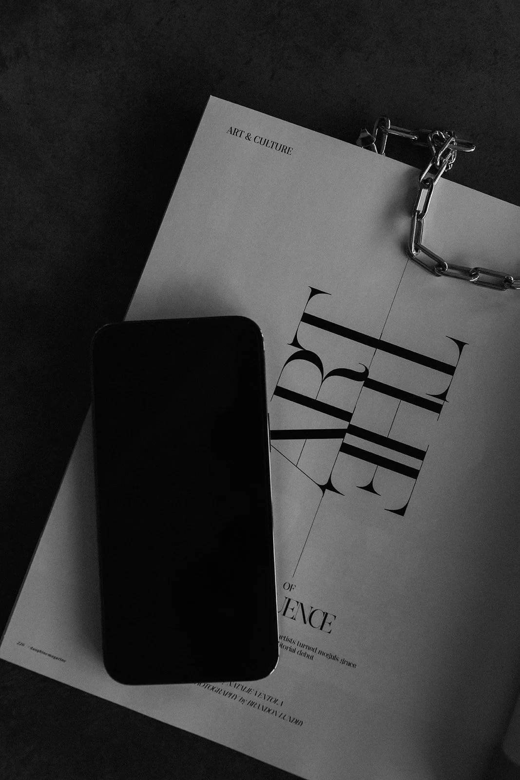 A black and white photo of a magazine or white paper that says ART and experience. On top of that is an iPhone