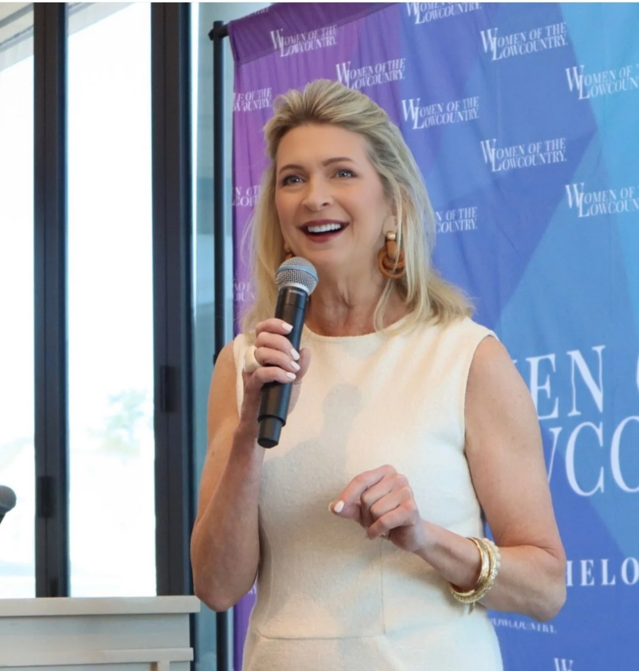 Kimberly Sundt speaking into a microphone, smiling, with a backdrop that reads 'Women of the Lowcountry'.