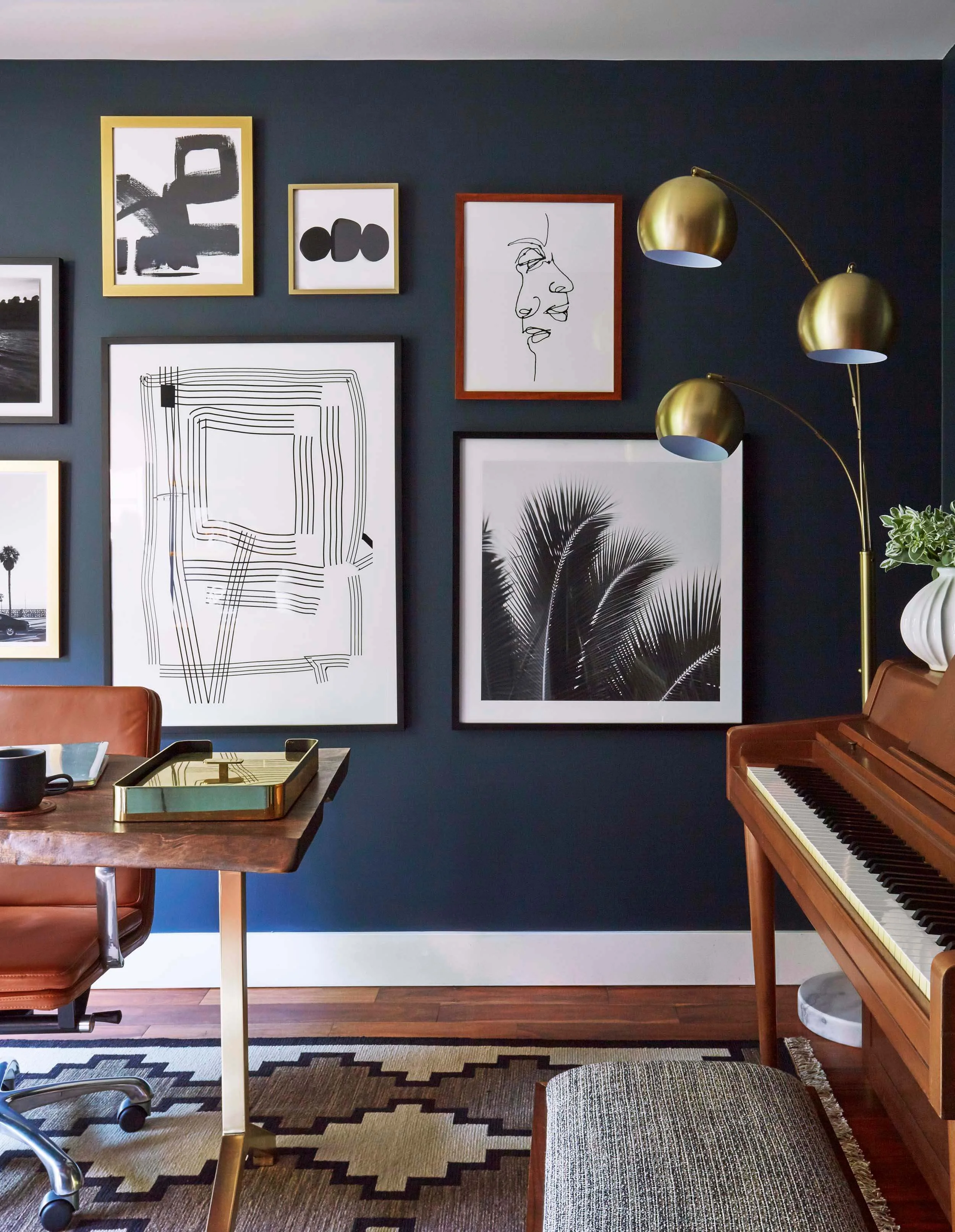 The brass finish of this lamp is picked up in the brass tray and legs of the desk, as well as the gold frames against the dark wall. This use of the lamp is anything but incidental. It’s carefully thought out and even works up a beautiful rhythm of curves with the palm tree in the image beside it. Image courtesy Ginny Macdonald Design.