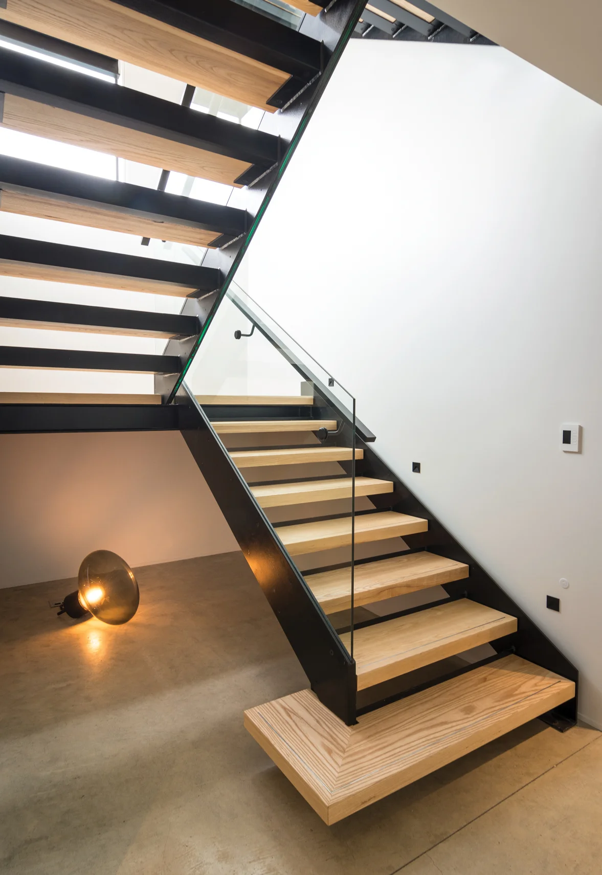 STAIRWELL: Feature Brokis Muffin floor lamp from ECC in smoke grey glass. Custom-steel, frameless glass and laminated American oak staircase.