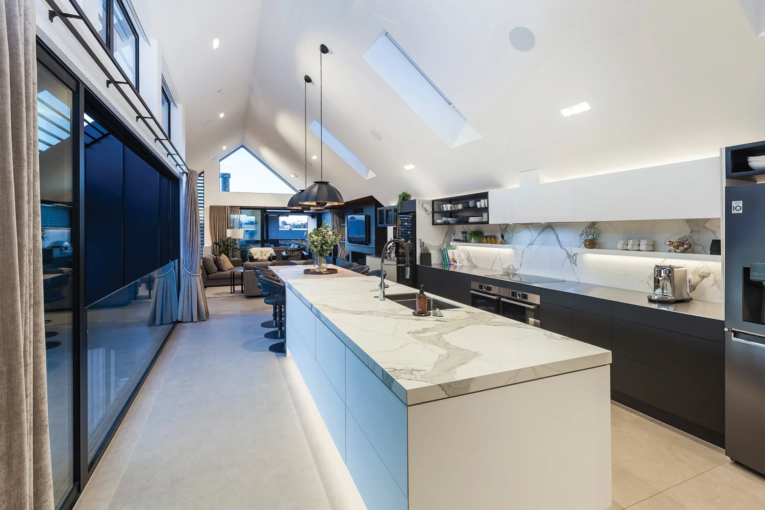 KITCHEN The sleek and spacious kitchen by MacKay Kitchens and Stairs incorporates doors and panels in Prime Laminate Black Velvet in soft matt, with the feature colour Prime Laminate Surrender in a soft matt finish. The benchtop is A-tech techno por…