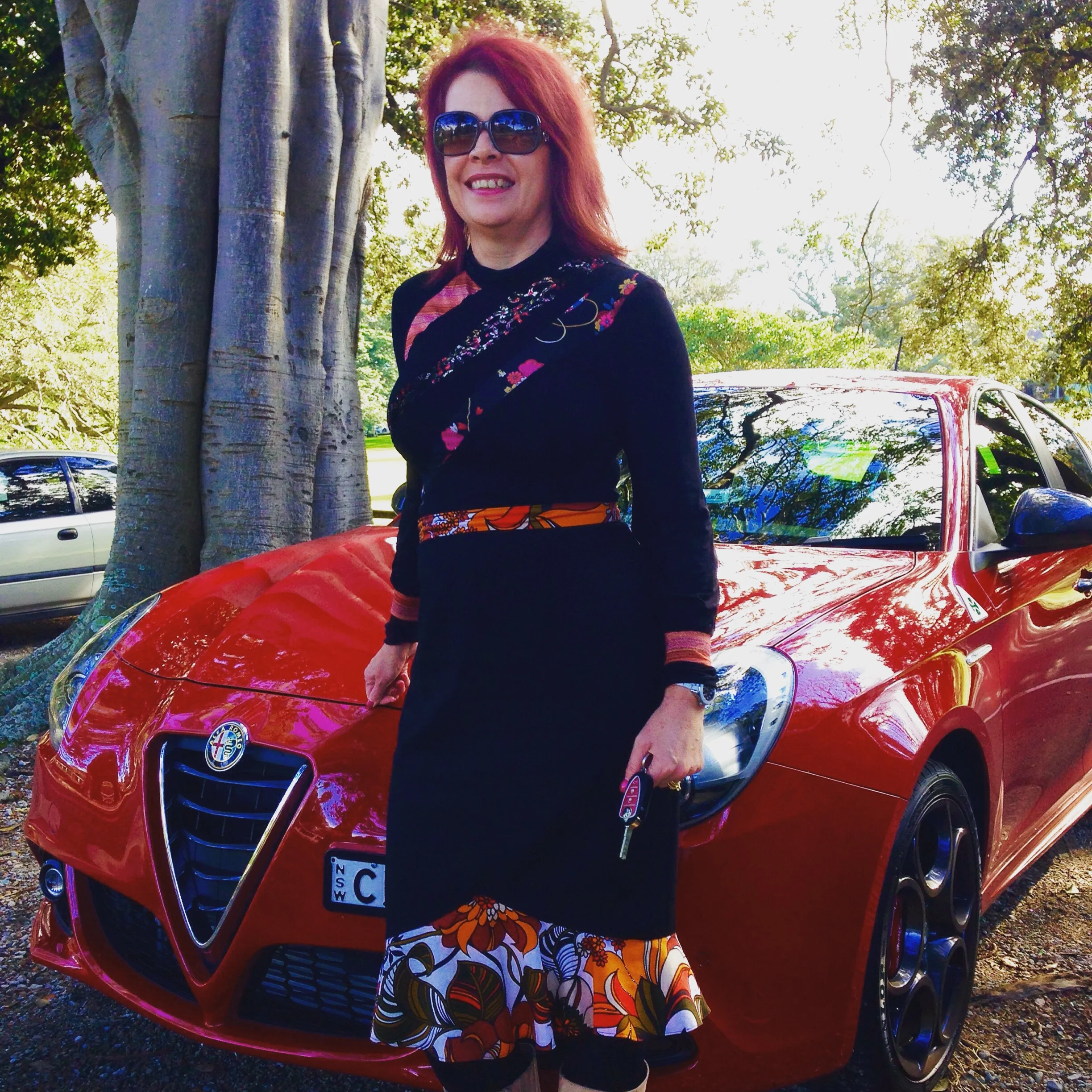 Lorelle wears a Penelope Red Jigsaw Skivvy Turtleneck Top in a black jersey knit with contrasting fabrics in shades of red, orange, brown, black and white.